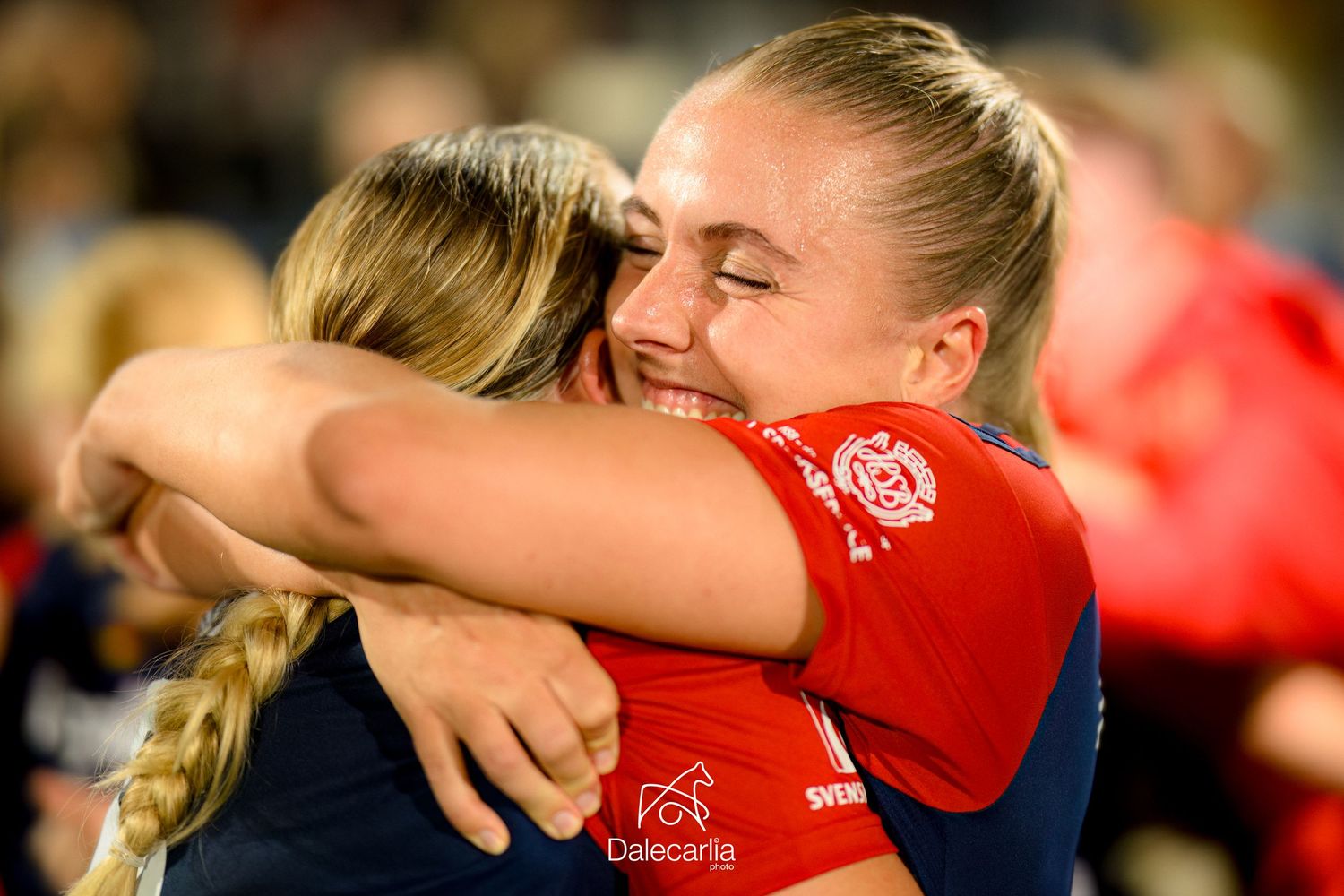 Two athletes in red and navy uniforms share an emotional embrace during a sporting celebration.