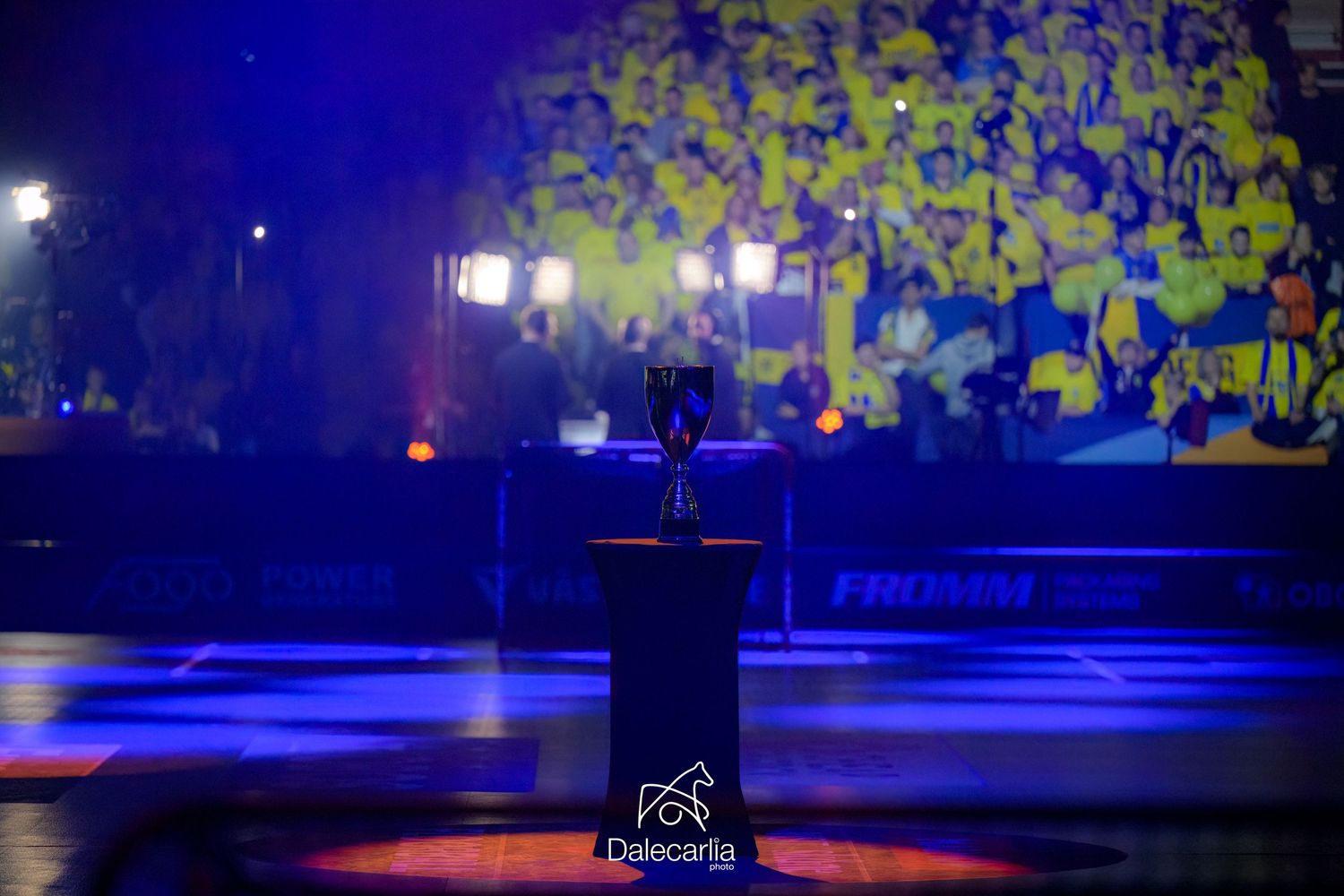 A microphone stands on an empty stage with blue lighting and a vibrant yellow backdrop projection.