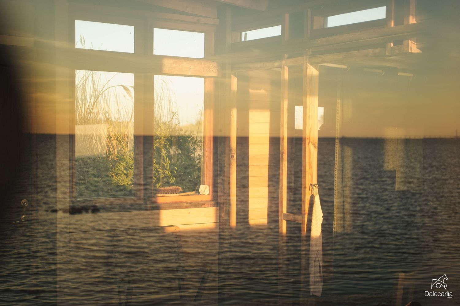 Double exposure of ocean waves and window frames create a dreamy sunset scene with golden light filtering through.