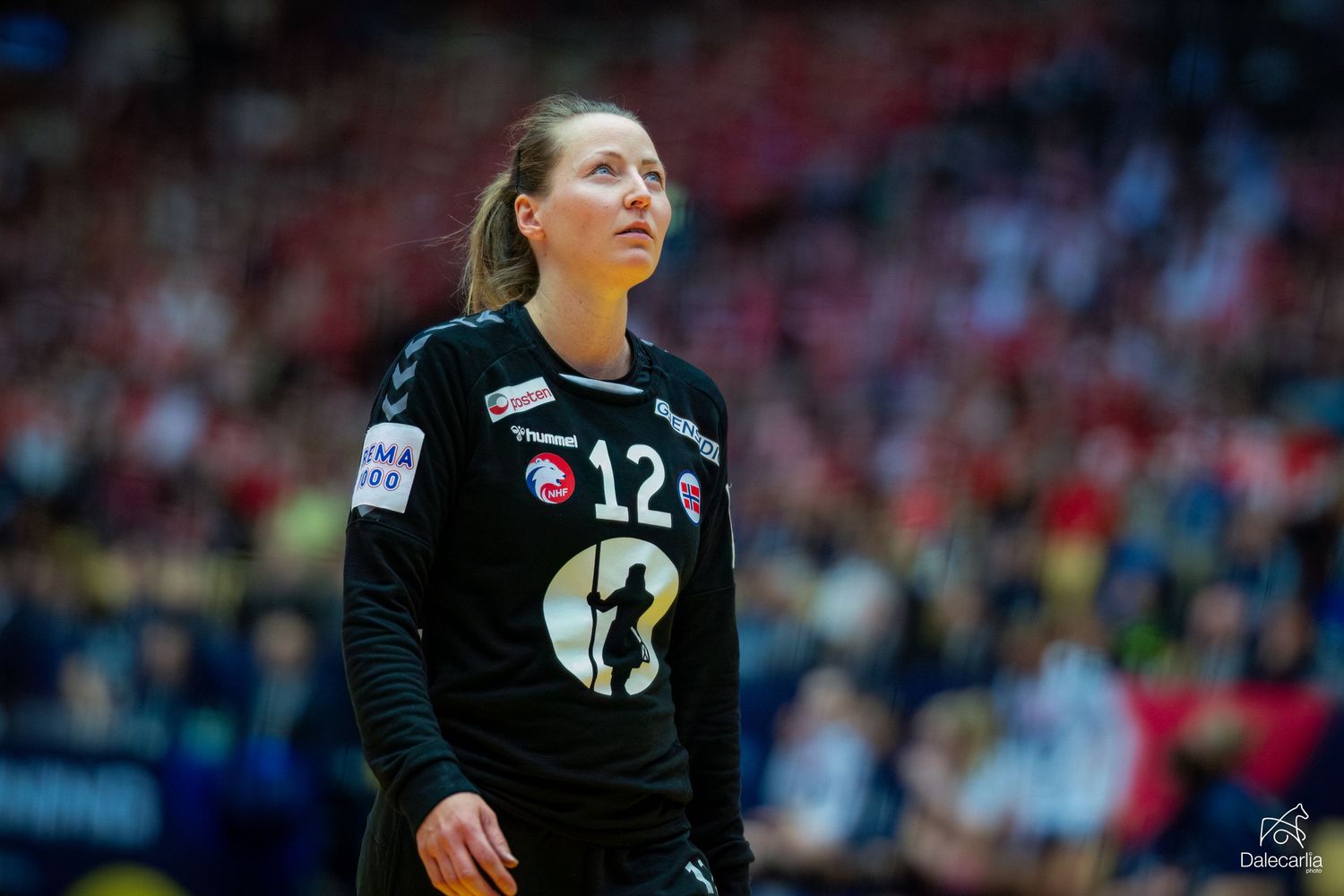 Female handball player in black number 12 jersey stands on court during professional match.
