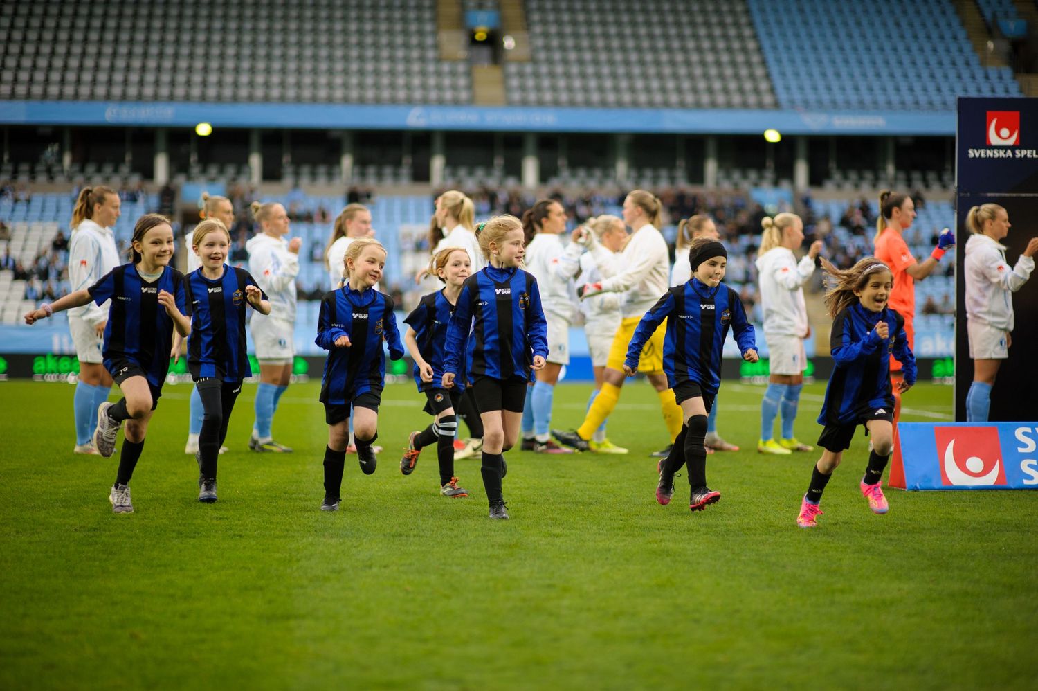 Youth soccer players in blue and white uniforms run together across a stadium field during a sporting event.