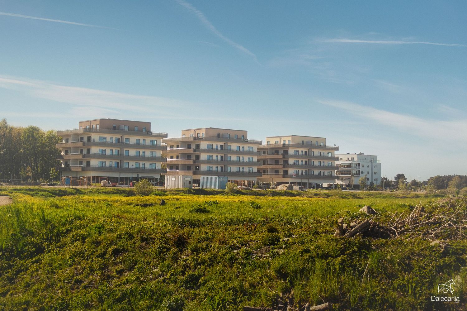 Modern luxury apartment buildings with white facades stand on a grassy hillside under a clear blue sky.