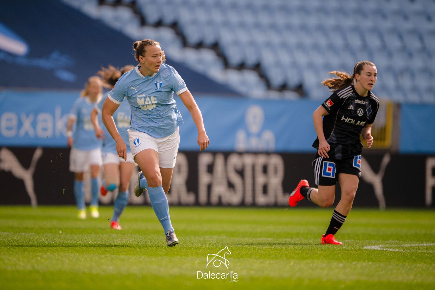 Women soccer players compete for the ball during a professional match on a stadium field in light and dark uniforms.
