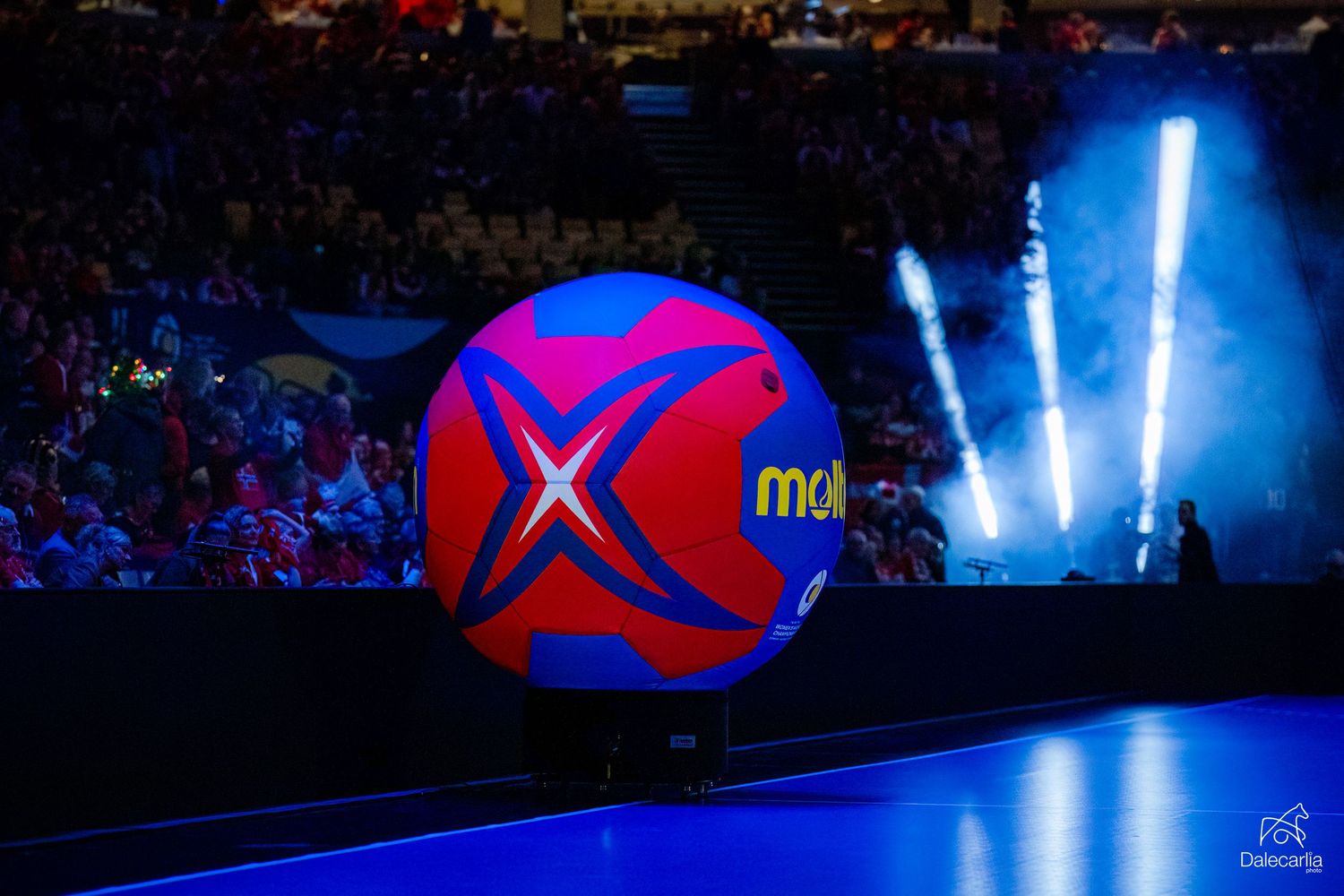 A colorful beach ball with a red X logo sits in the foreground against a dark arena with blue lighting effects.