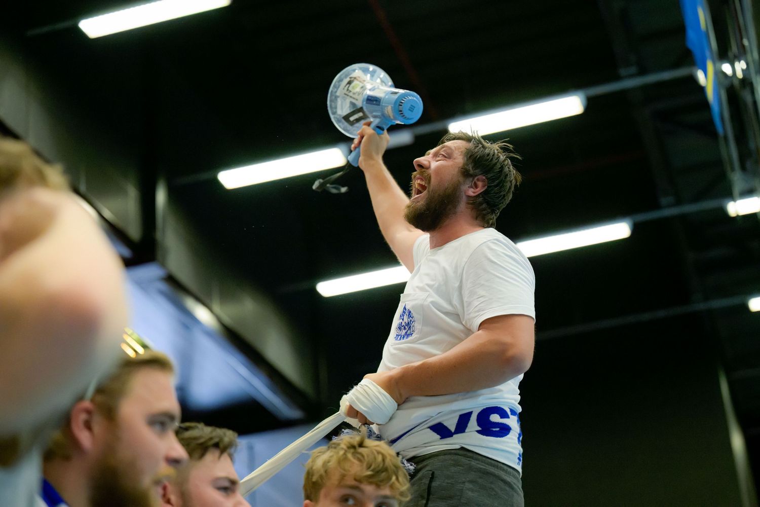 Someone in a white t-shirt takes a drink from a water bottle during what appears to be a sporting event.