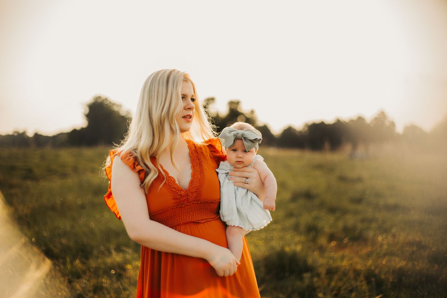 Woman in orange dress laughs joyfully in sunlit field during golden hour.