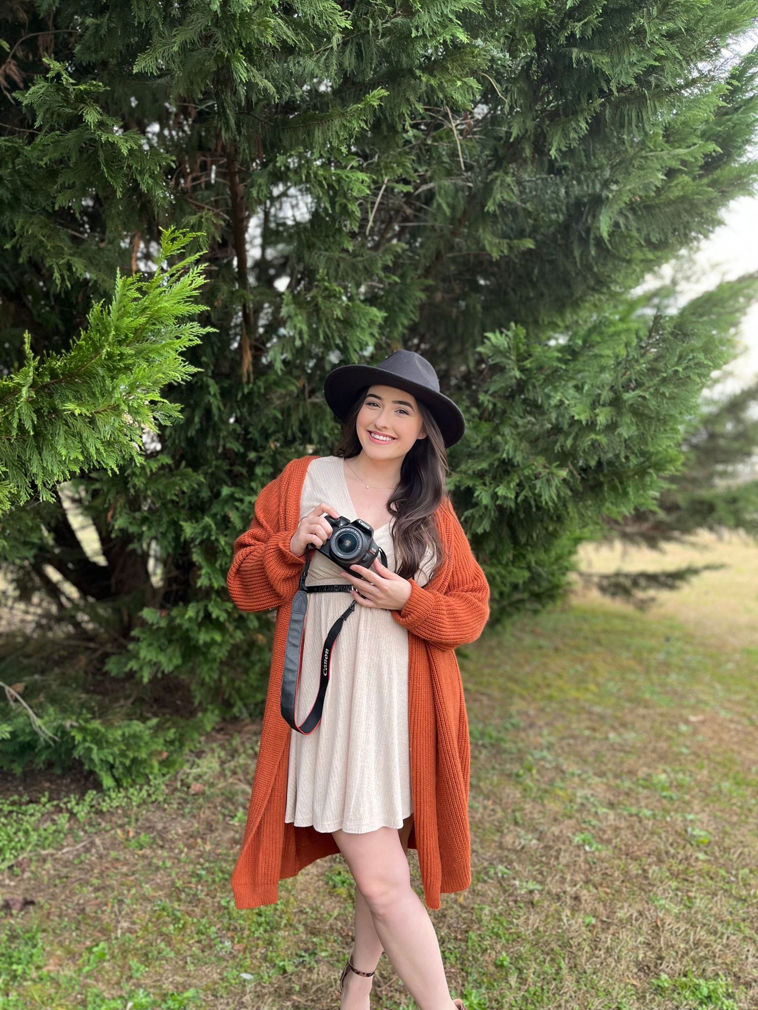 Woman holding a camera standing against a tree line in Albertville Alabama