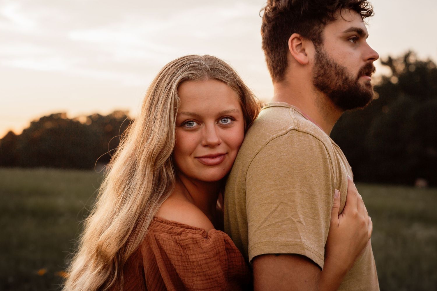 Romantic couple portrait at sunset in field with warm lighting.