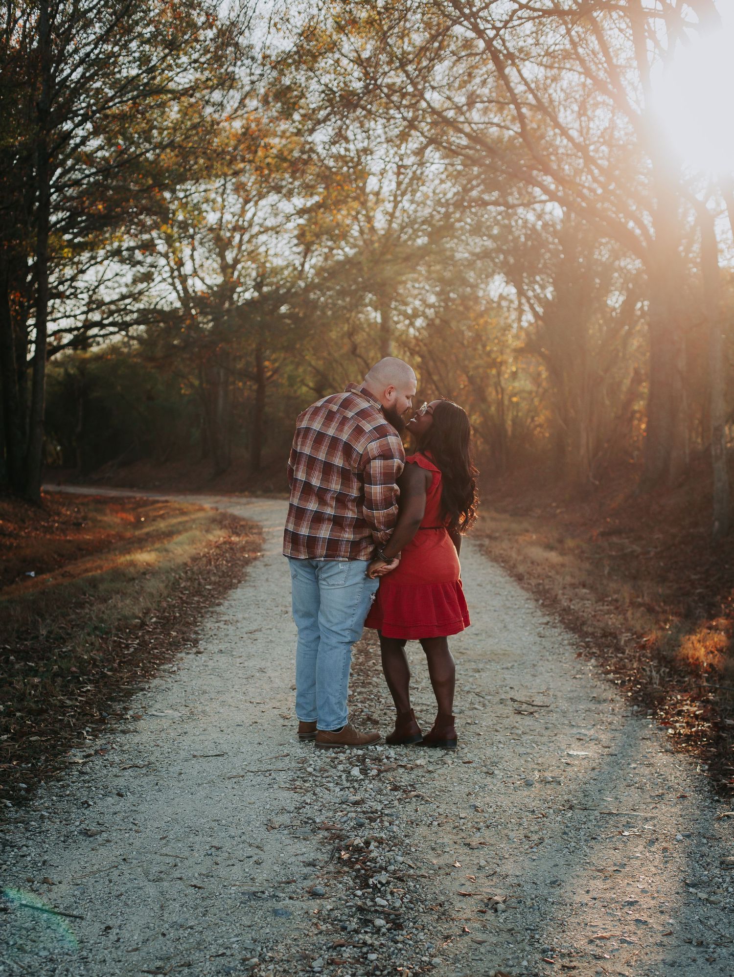 Couple sharing an intimate moment on a sunlit autumn path through the woods.