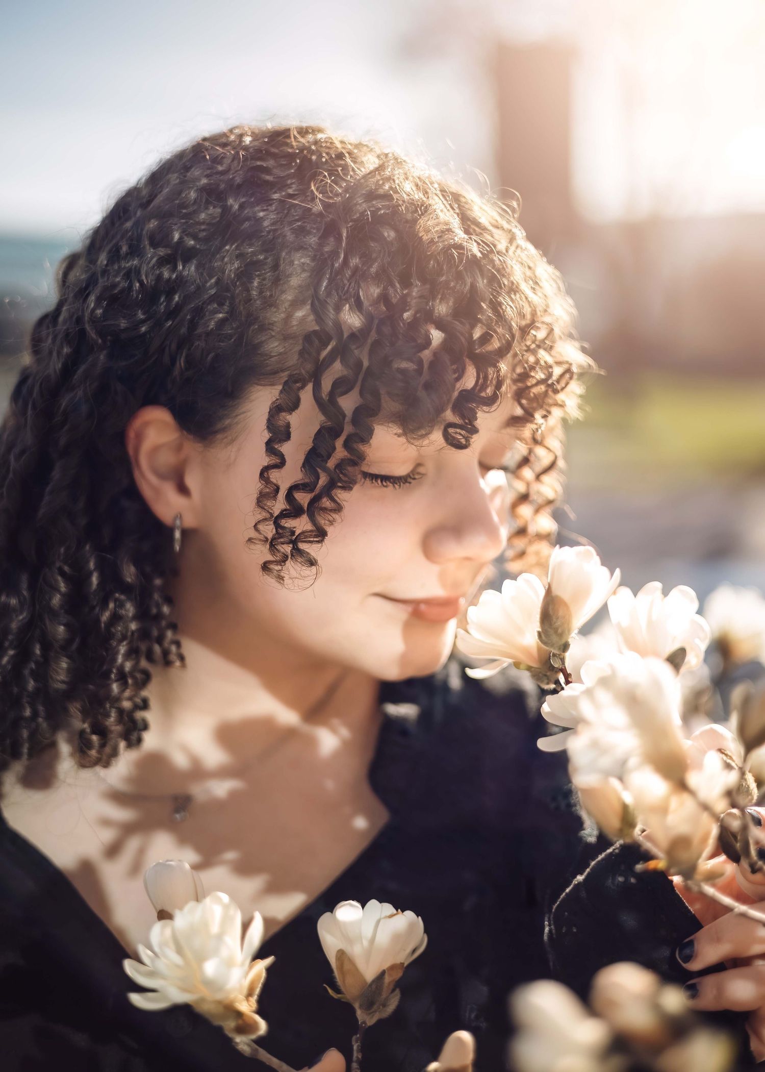A portrait of a person with curly hair smelling white flowers in soft sunlight with a dreamy effect.