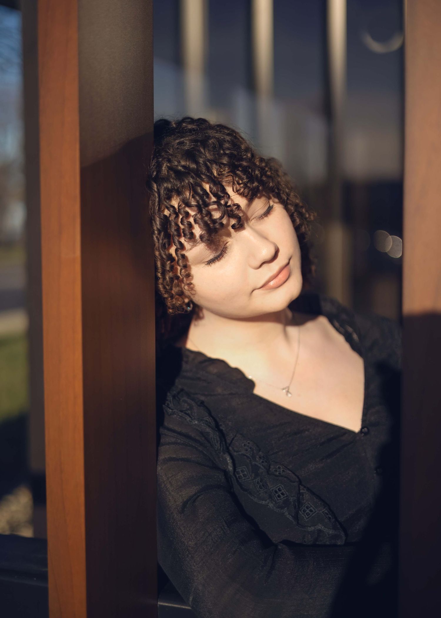 Portrait photo of someone with curly brown hair wearing a shirt, captured in warm evening lighting at sunset.