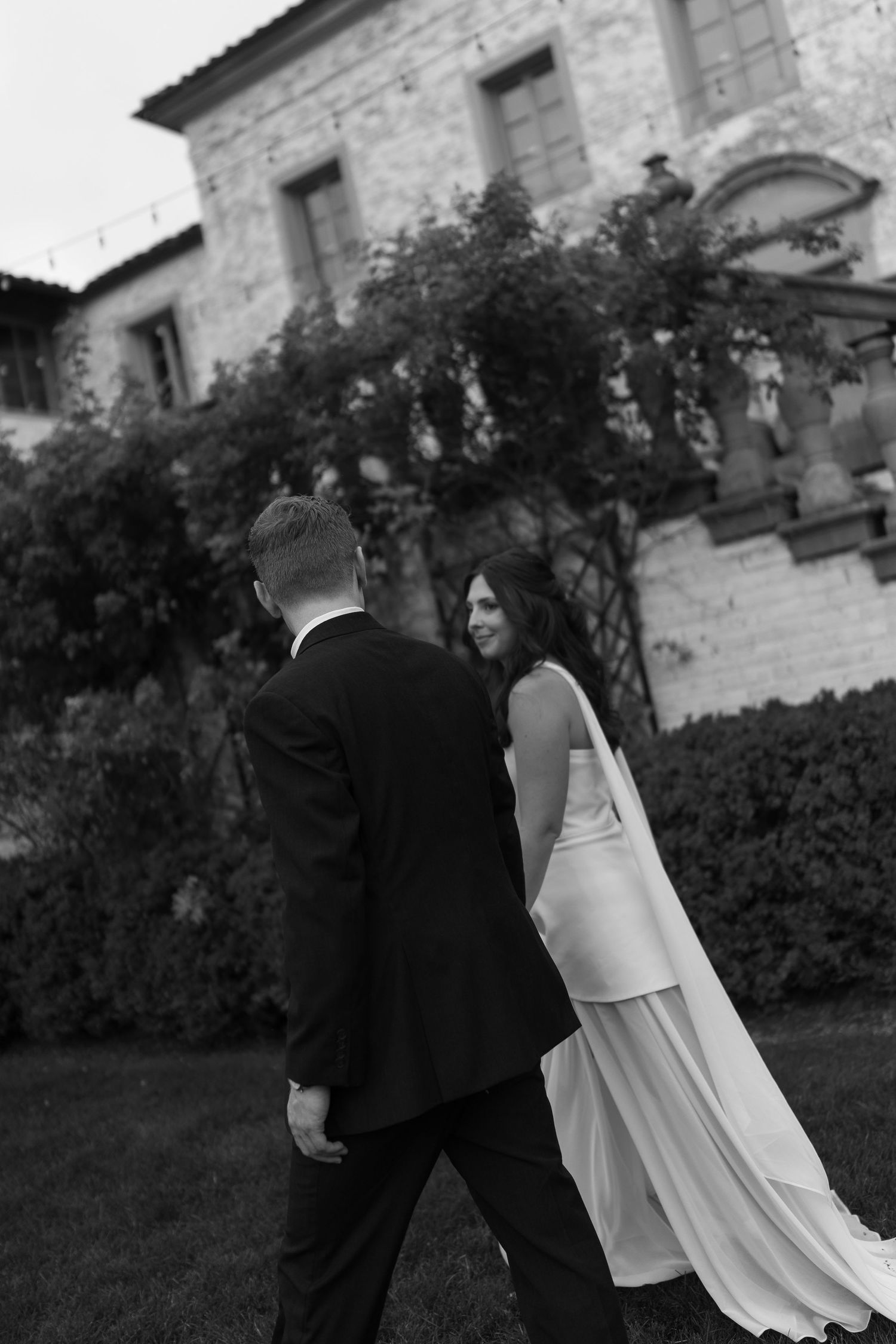 A black and white portrait of a couple walking through a rustic stone garden setting.