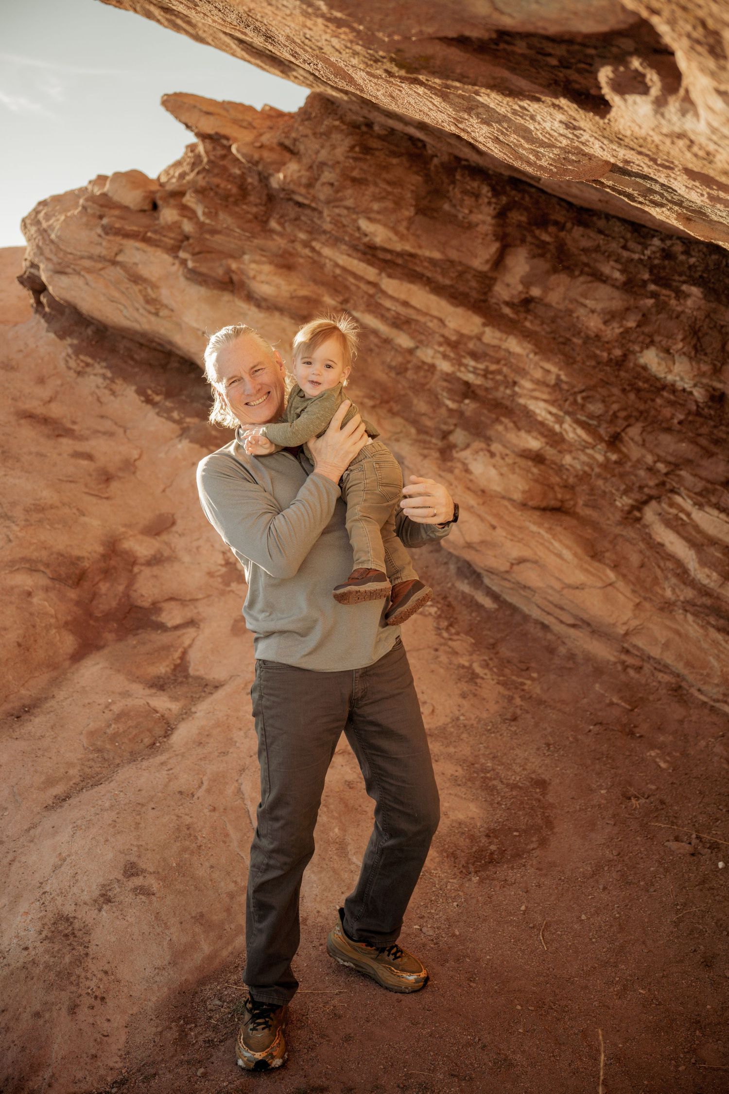 Hiker in grey sweater stands against red rock canyon wall at sunset.
