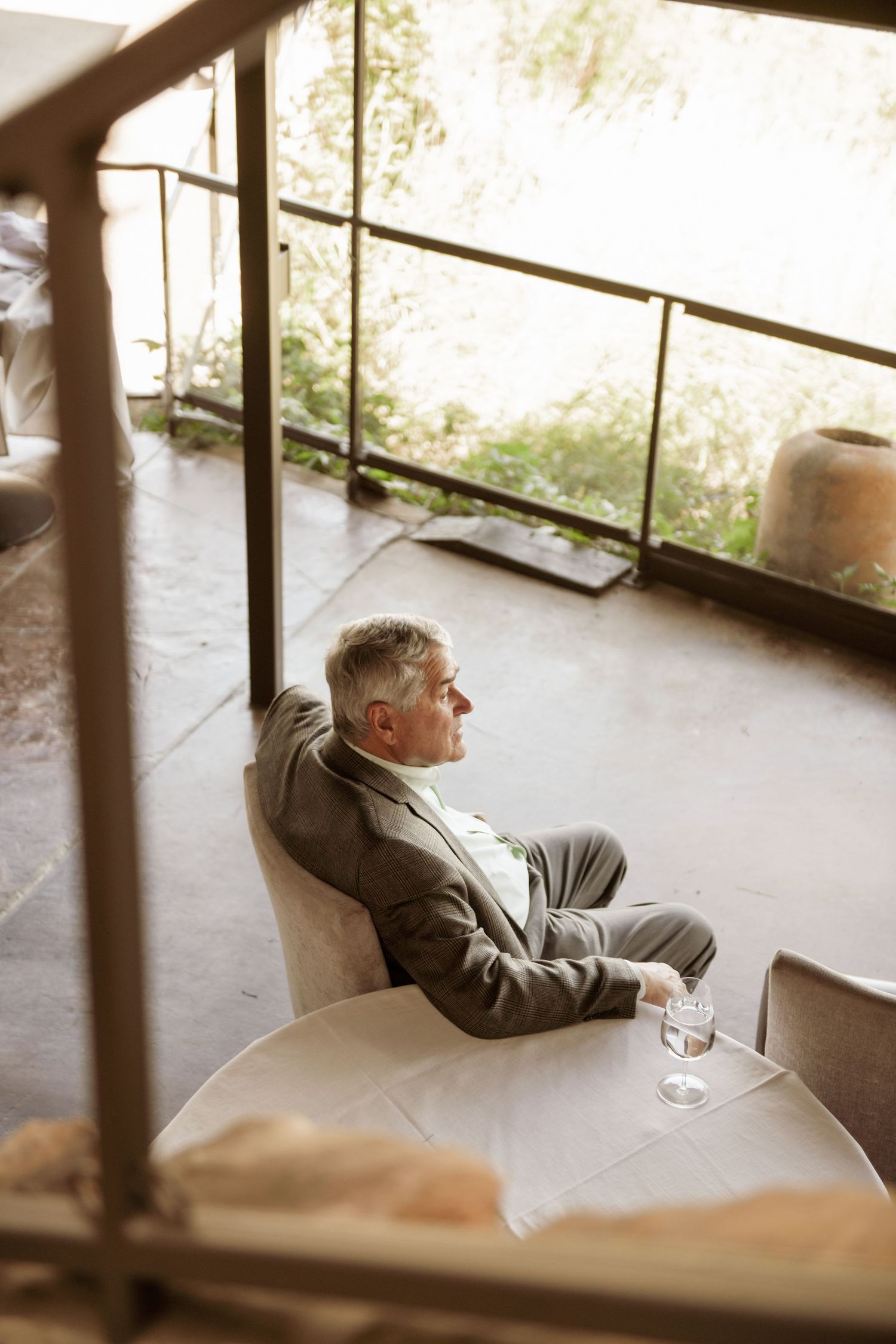 Person relaxing in grey armchair on balcony with glass of water on sunny afternoon.
