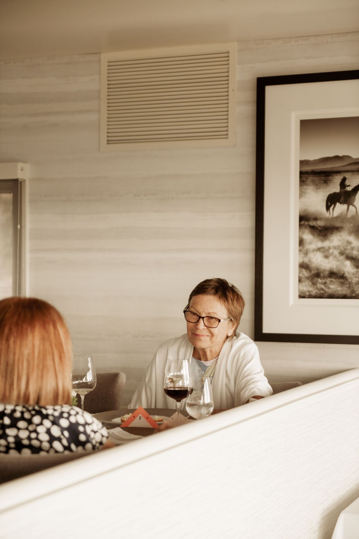 Two people share conversation and red wine at a cozy restaurant with black and white western art on the wall.