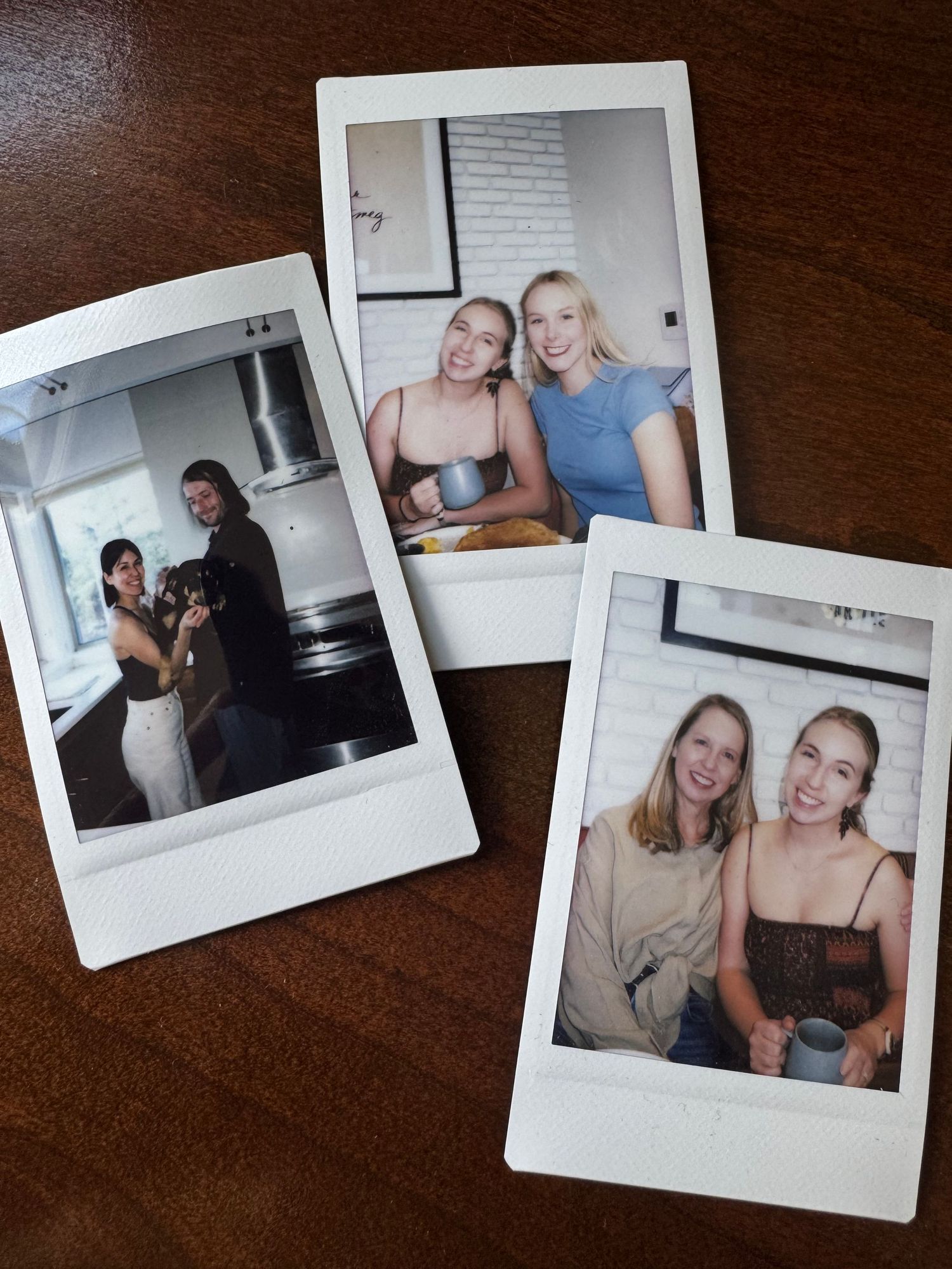 Three polaroid photos spread out on a dark wooden surface showing people gathering together indoors.