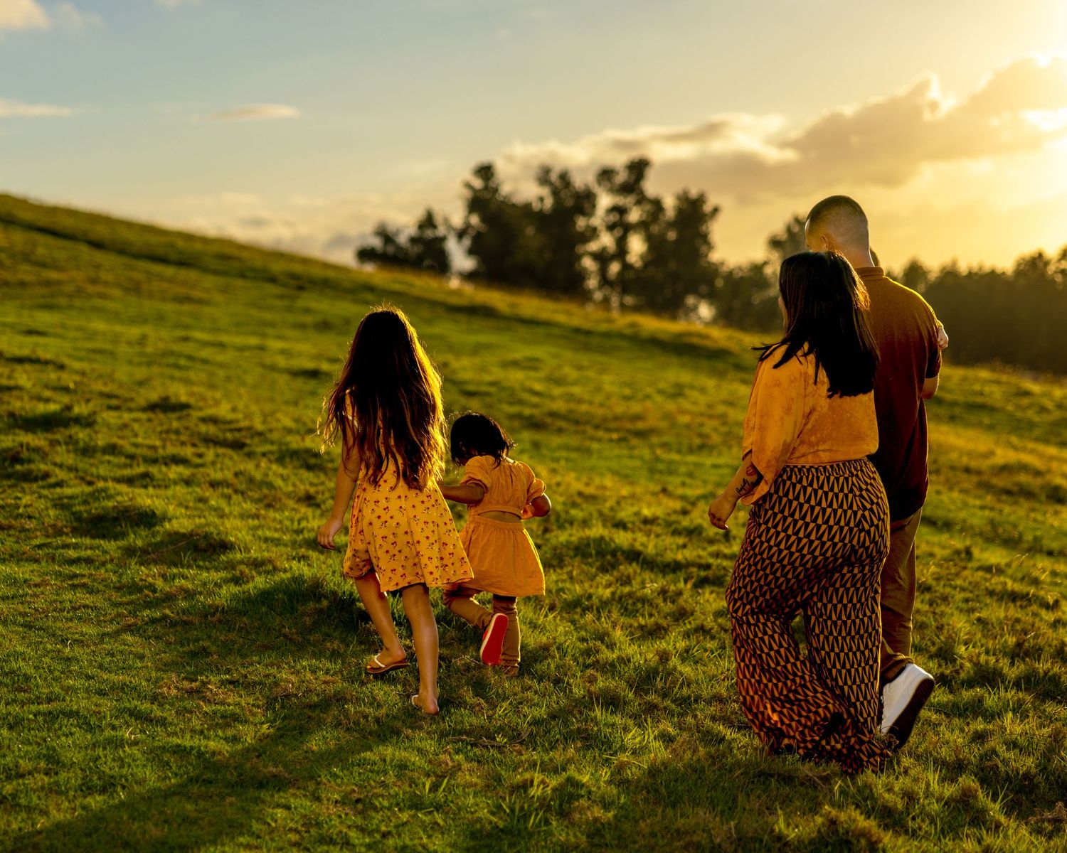 Silhouettes of family walking on grassy hill during golden sunset.