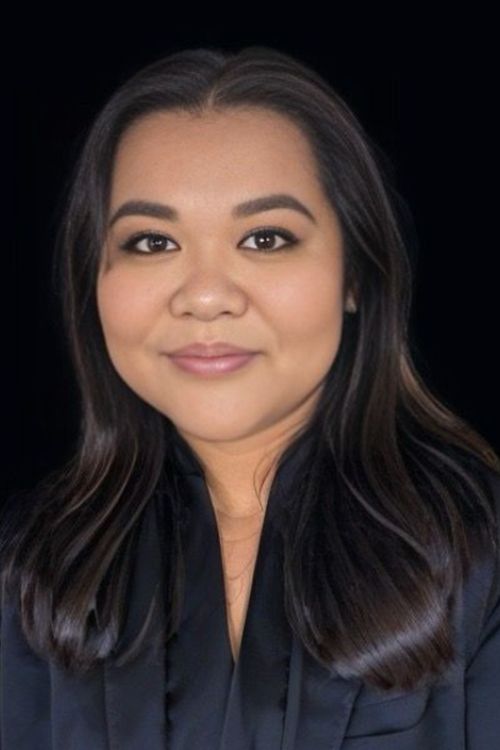 Professional headshot of co-owner with long dark hair wearing black outfit against dark background.