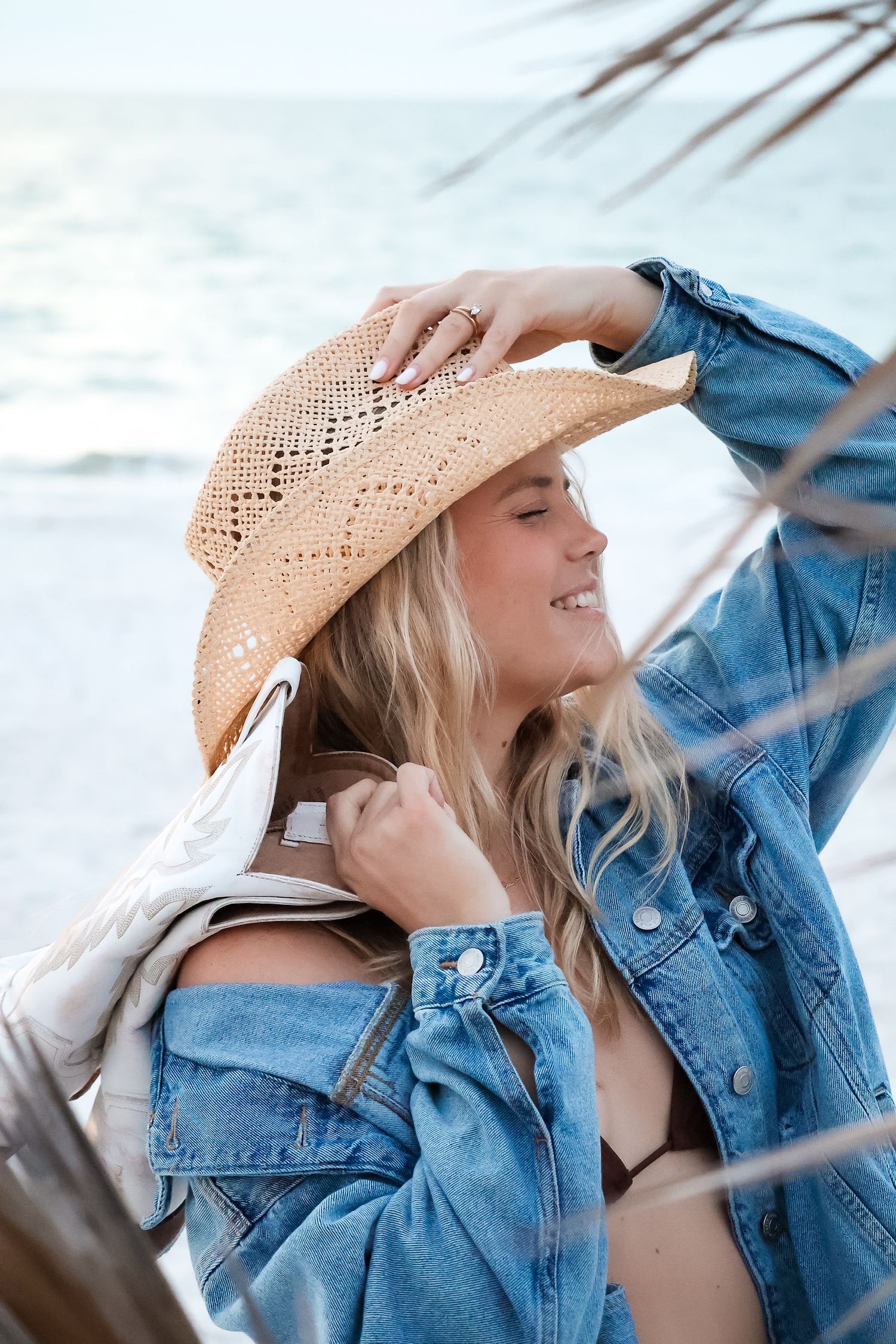 Person in denim jacket and straw hat enjoying a sunny beach day.