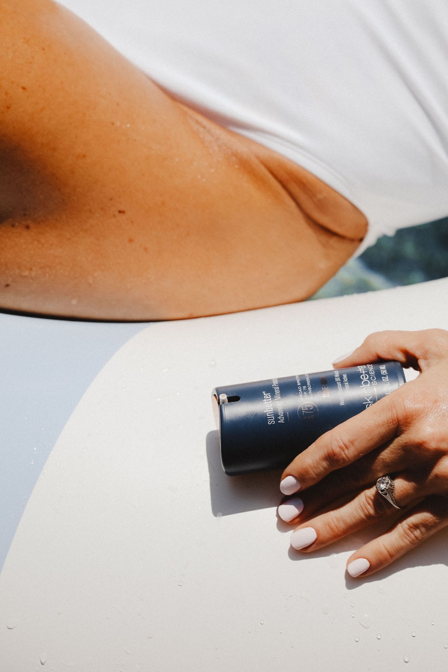 Hand wearing rings holds a dark blue beauty product container against a white background.