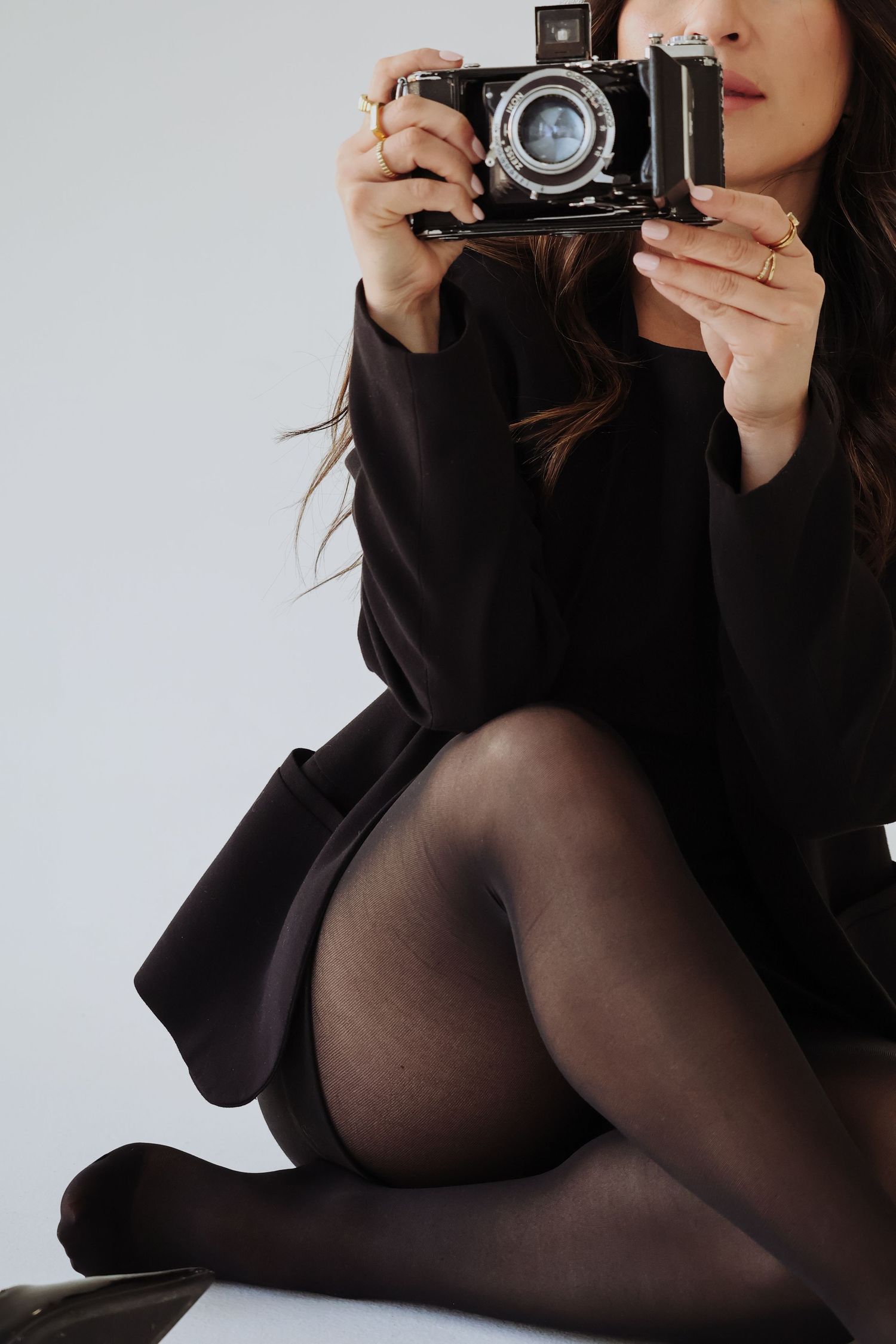 Person holding vintage camera wearing black clothing against white background.