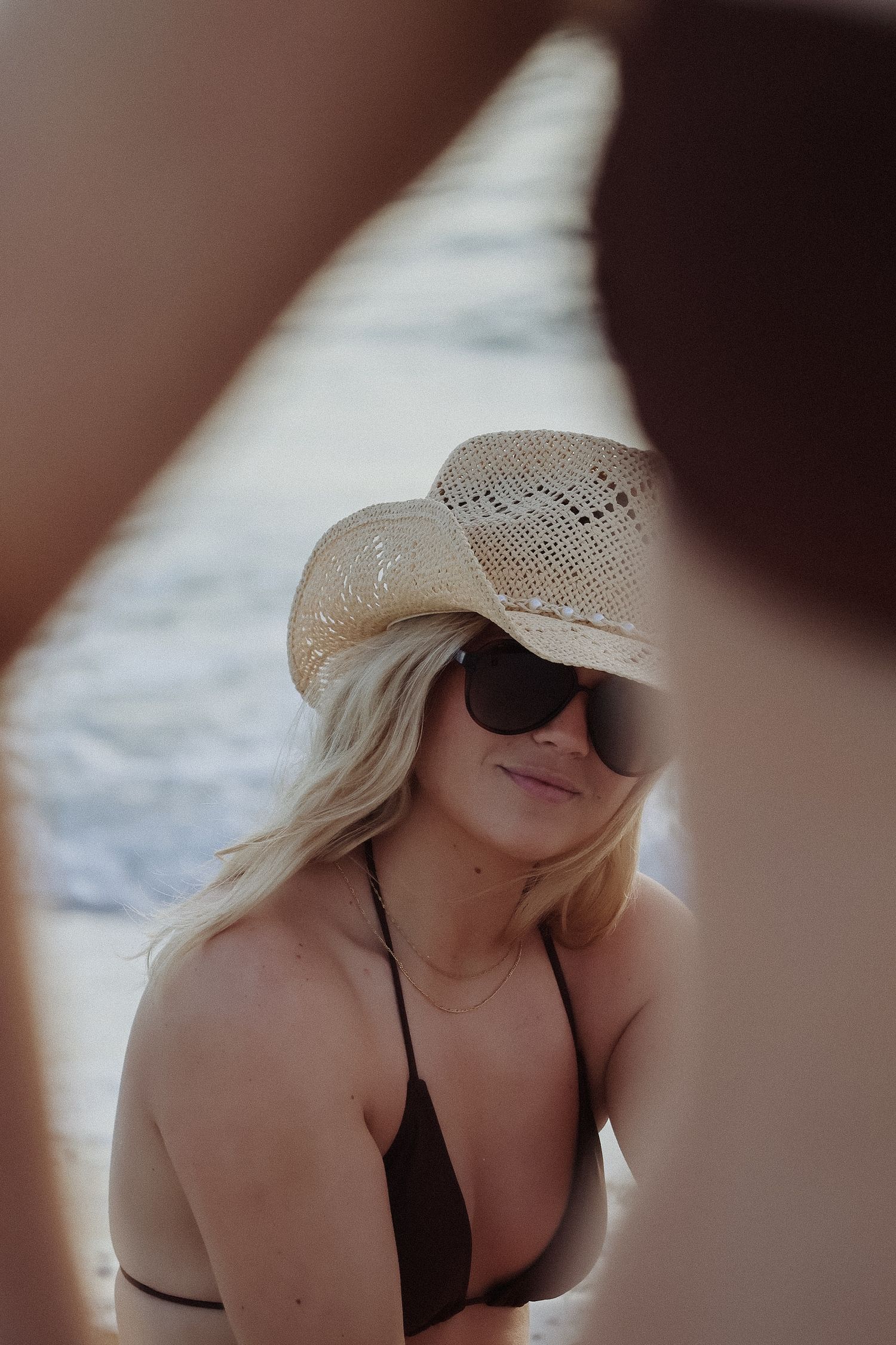 Person wearing straw cowboy hat and sunglasses in moody lighting.