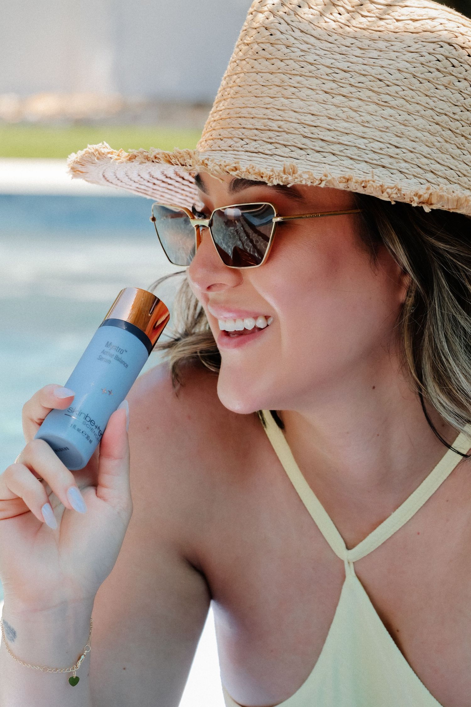 Summer portrait of person in swimwear holding blue bottle with straw hat and sunglasses.