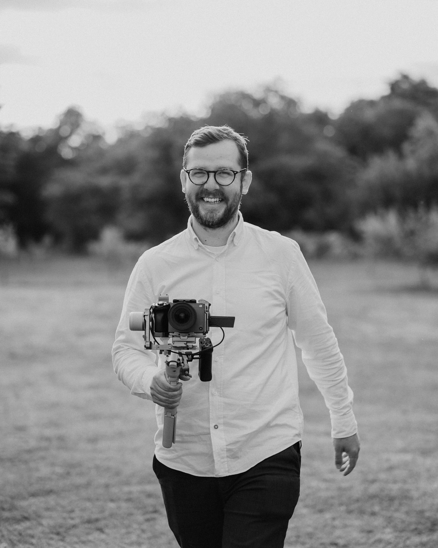 Black and white photo of a photographer walking in a field while carrying a professional camera gimbal setup.