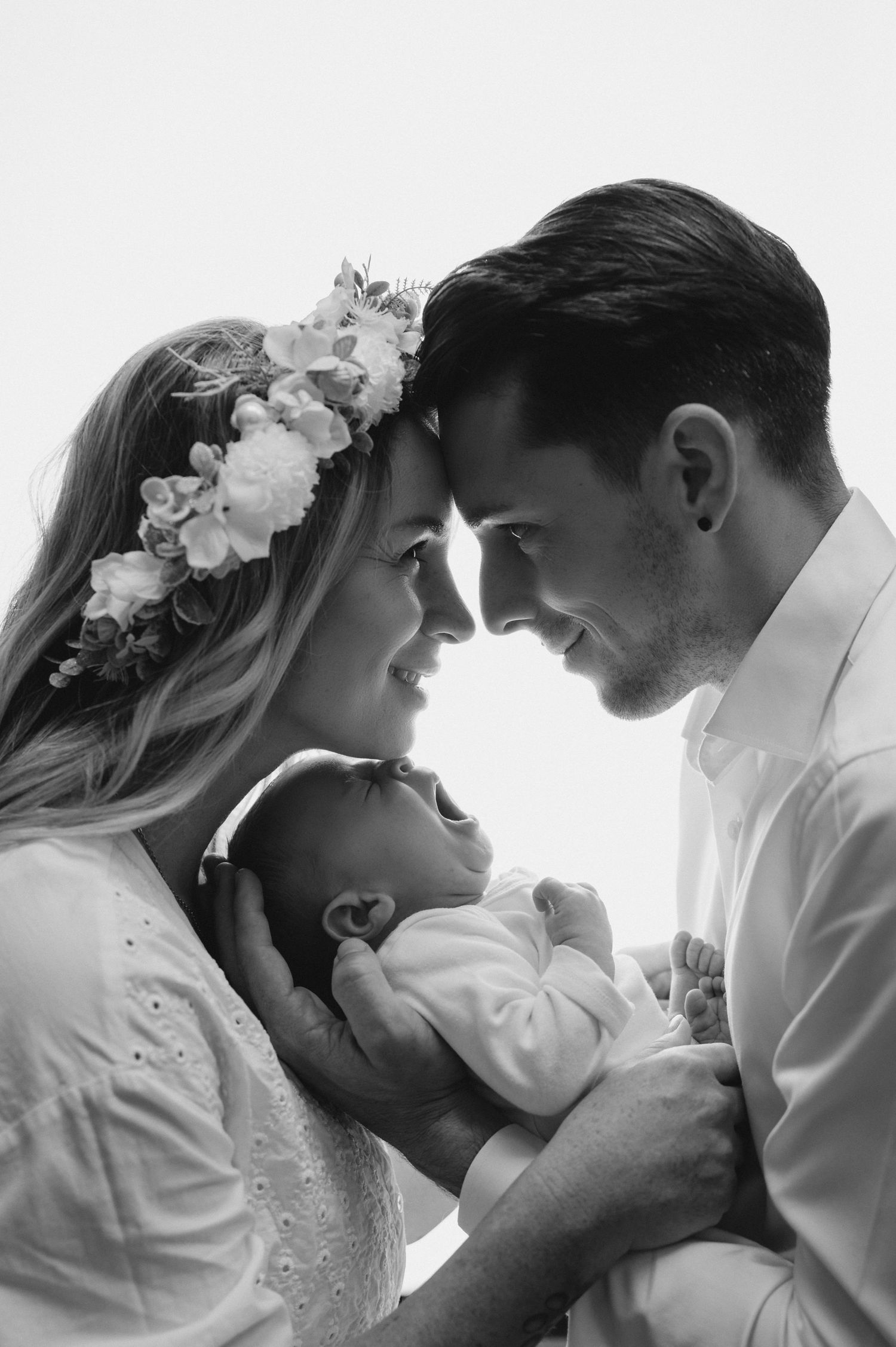 A romantic black and white portrait of parents in wedding attire holding their newborn close.