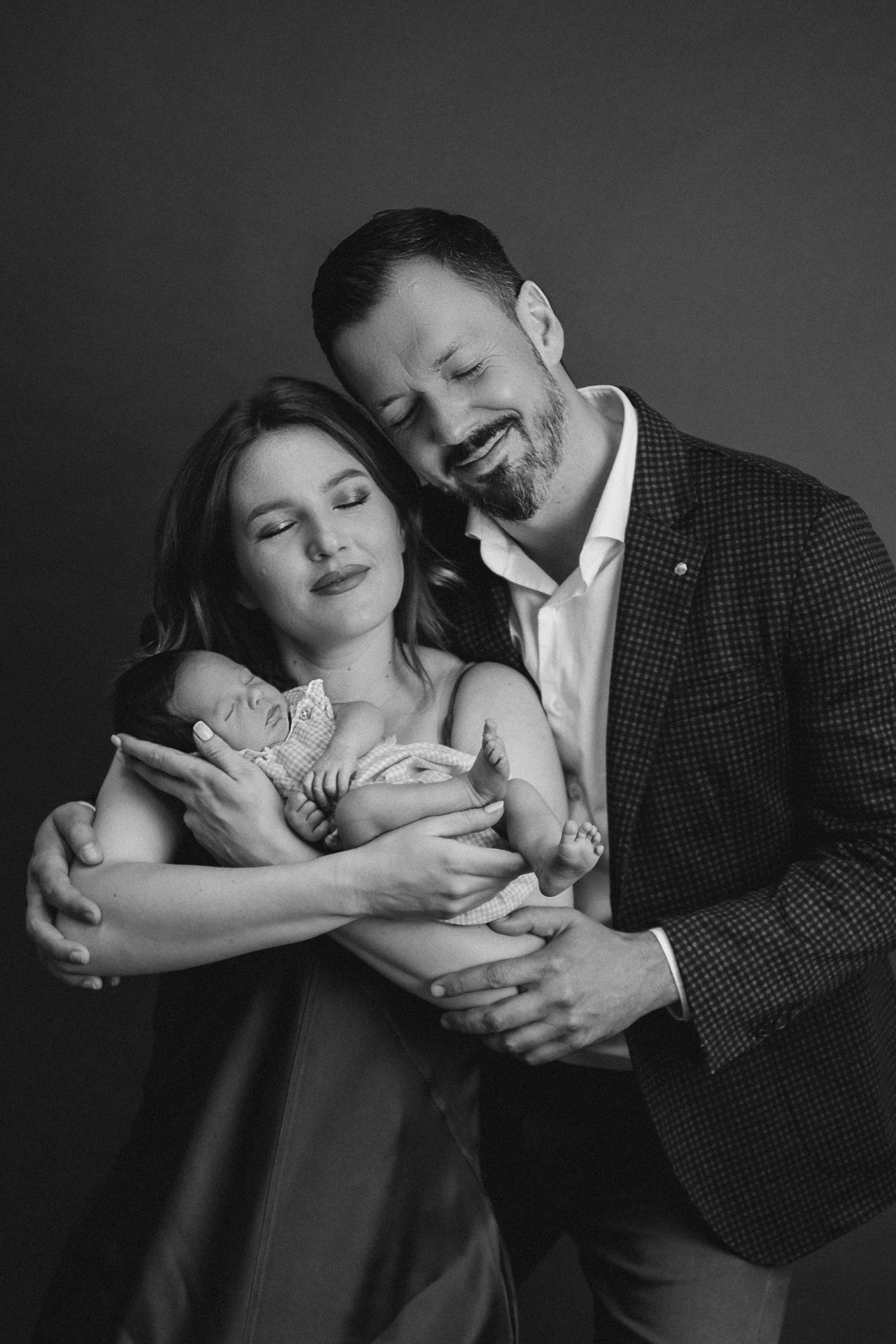 Black and white studio portrait of couple embracing with baby.
