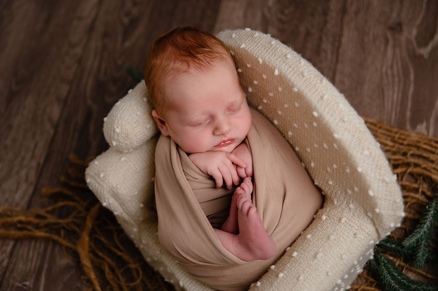 Peaceful sleeping newborn wrapped in beige fabric resting in dotted white blanket-lined basket.