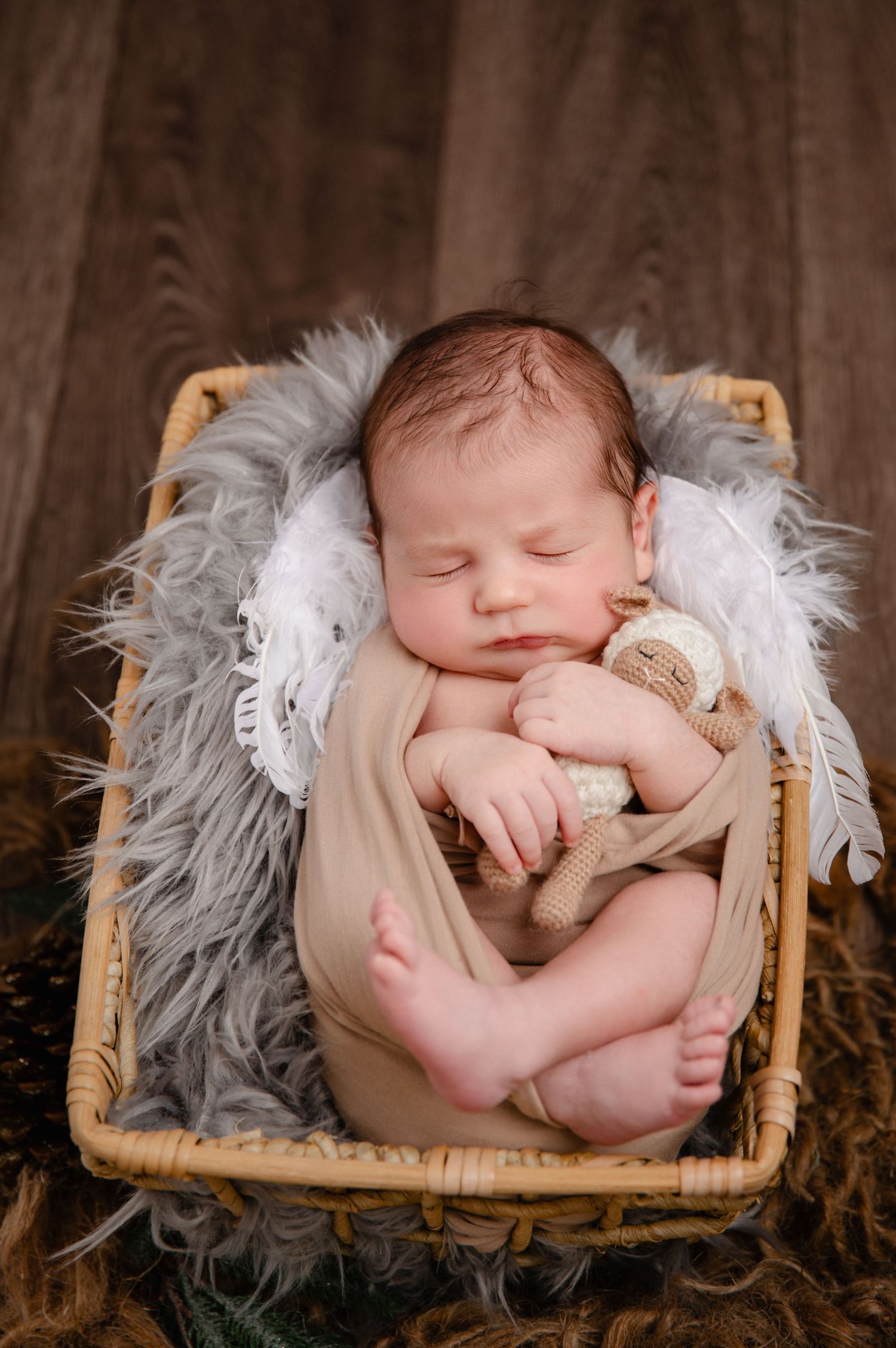 Sleeping newborn on grey fur in wicker basket holding small teddy bear.