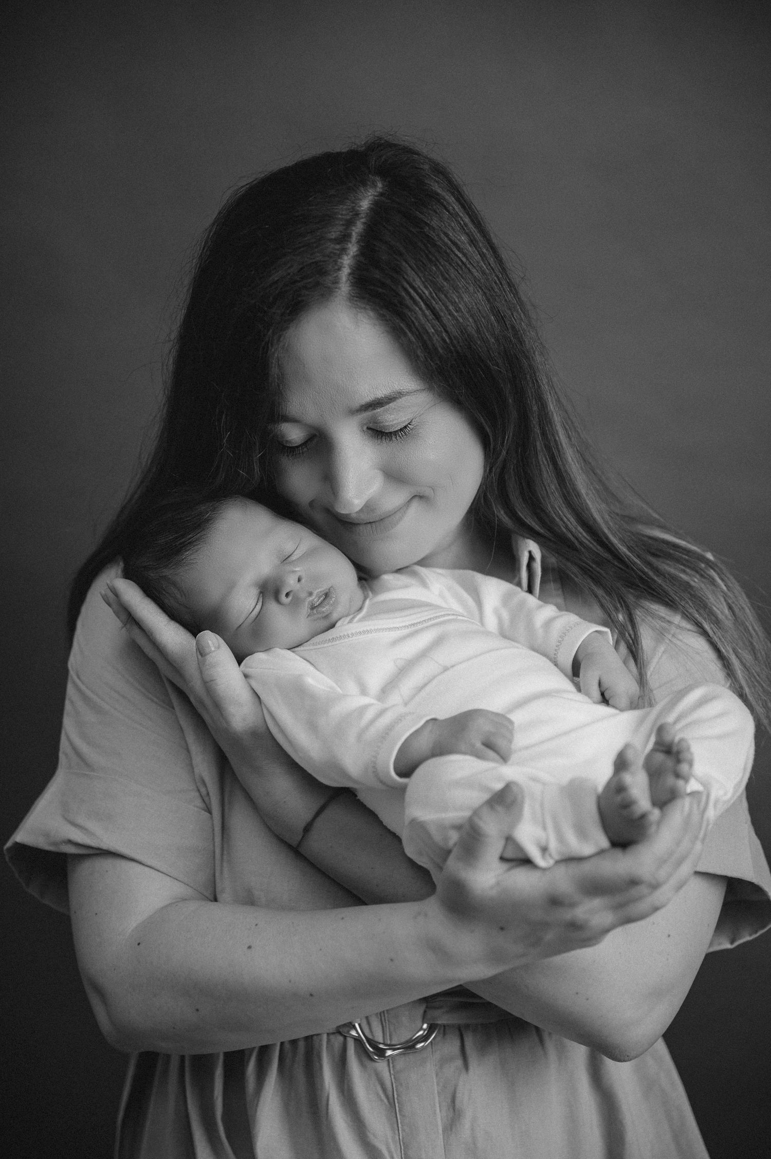 Black and white portrait of mother cradling sleeping newborn baby.