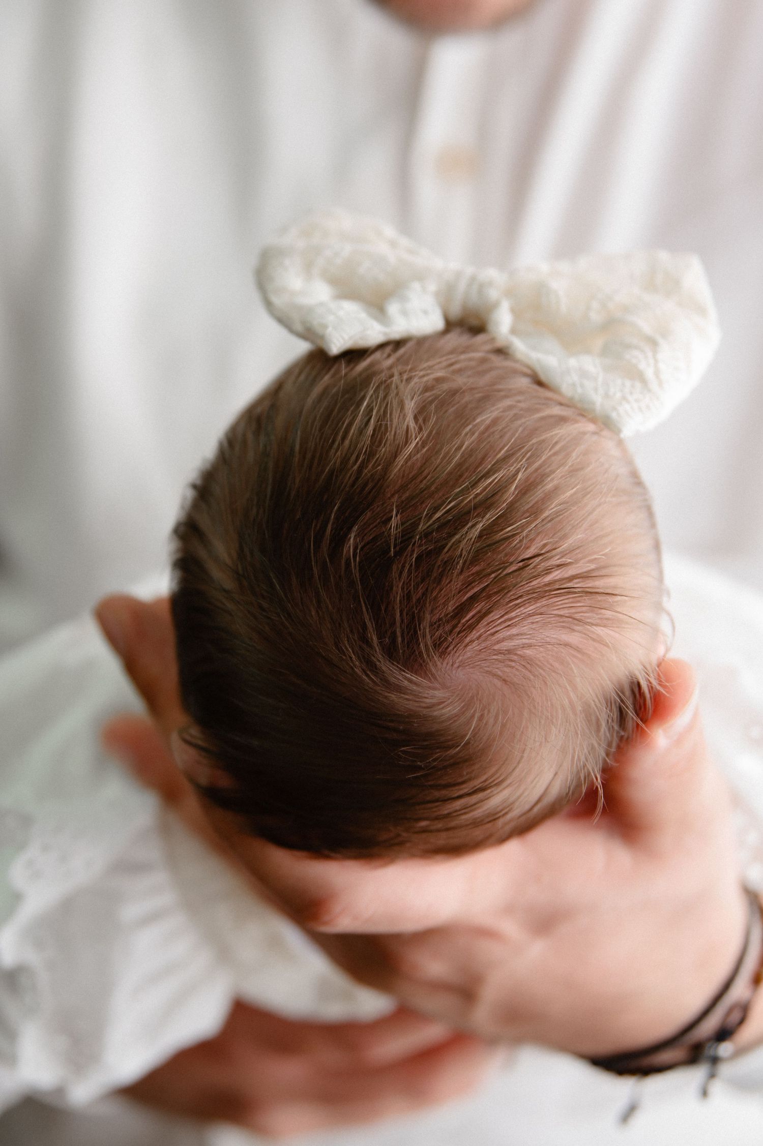 Close-up detail shot of a baby's head wearing a white lace bow.