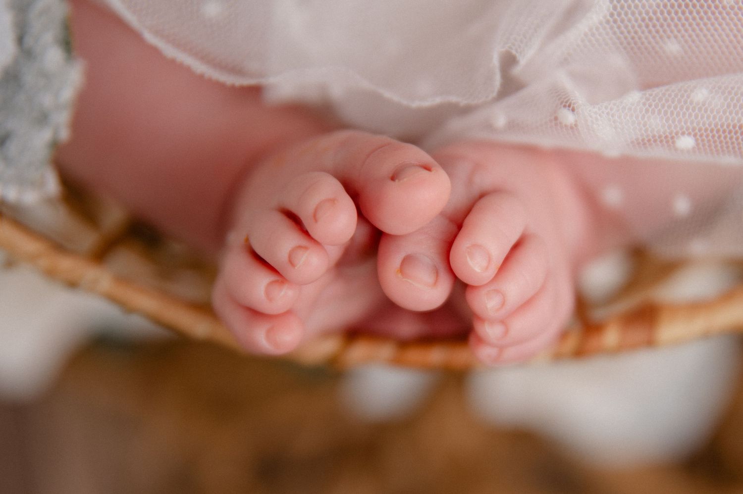 Close-up photograph of tiny newborn baby feet beneath white lace fabric.