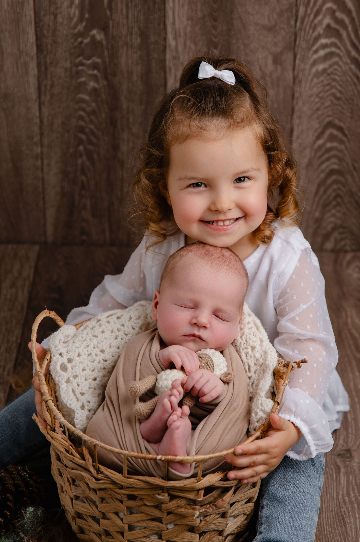 Sweet sibling moment as older child holds wicker basket containing sleeping newborn.