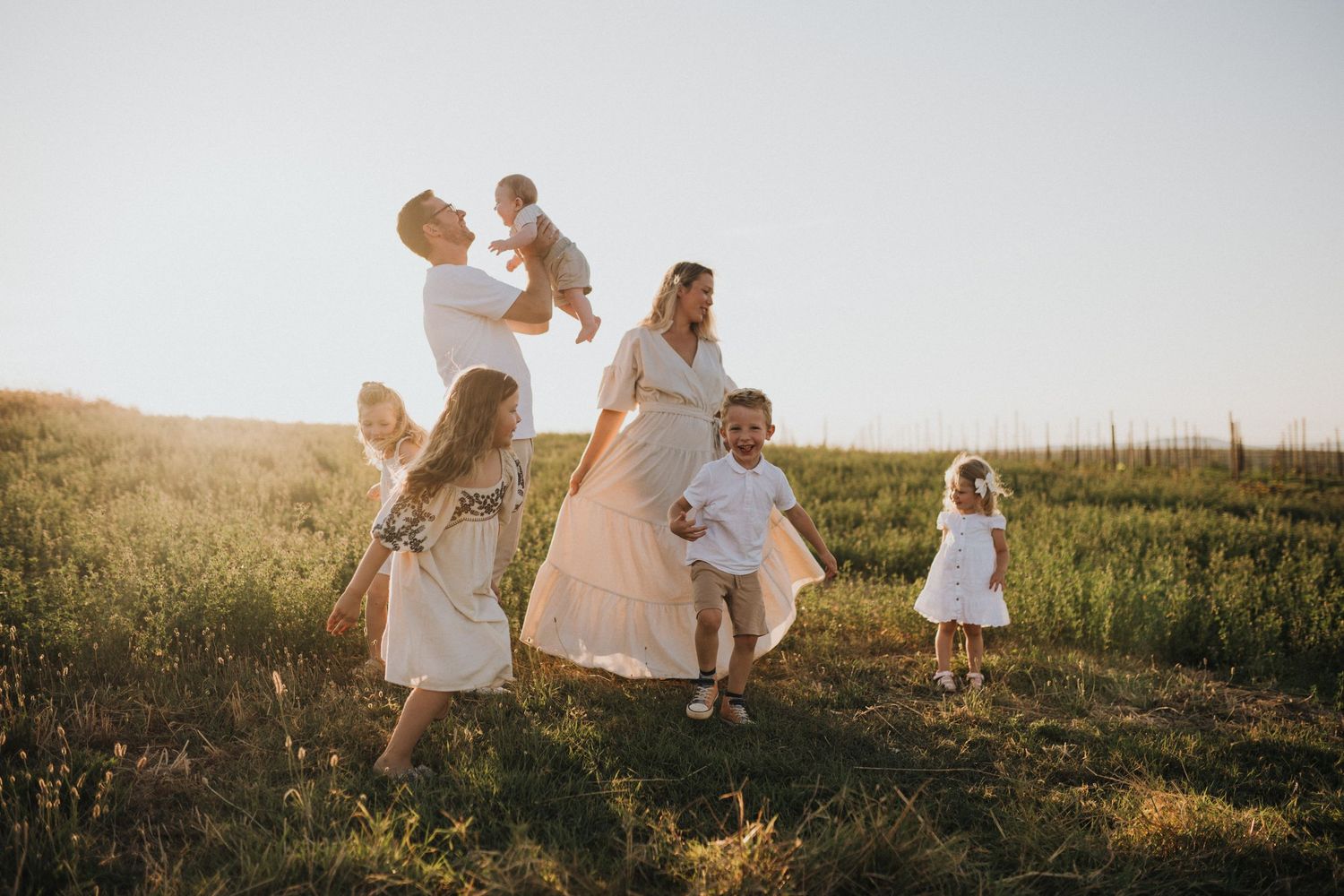 Family enjoys playful moment together in golden sunlit field during sunset photoshoot.