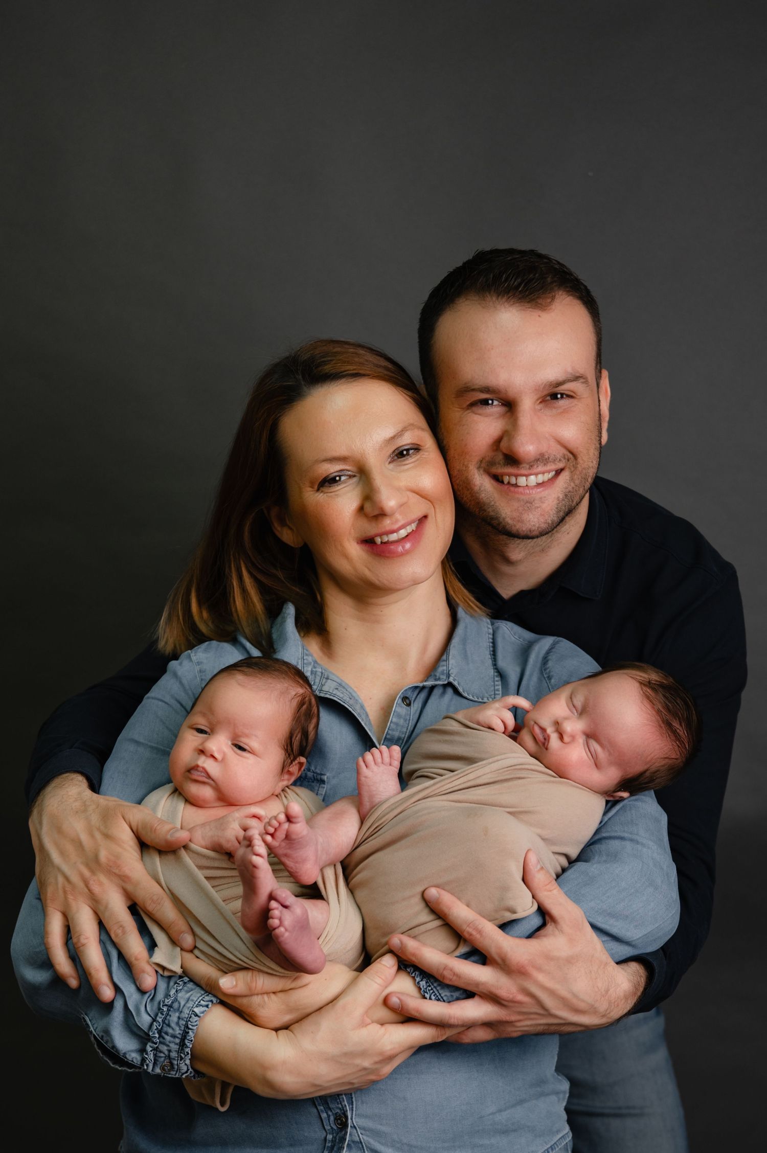 Parents holding twin newborn babies in professional studio setting.