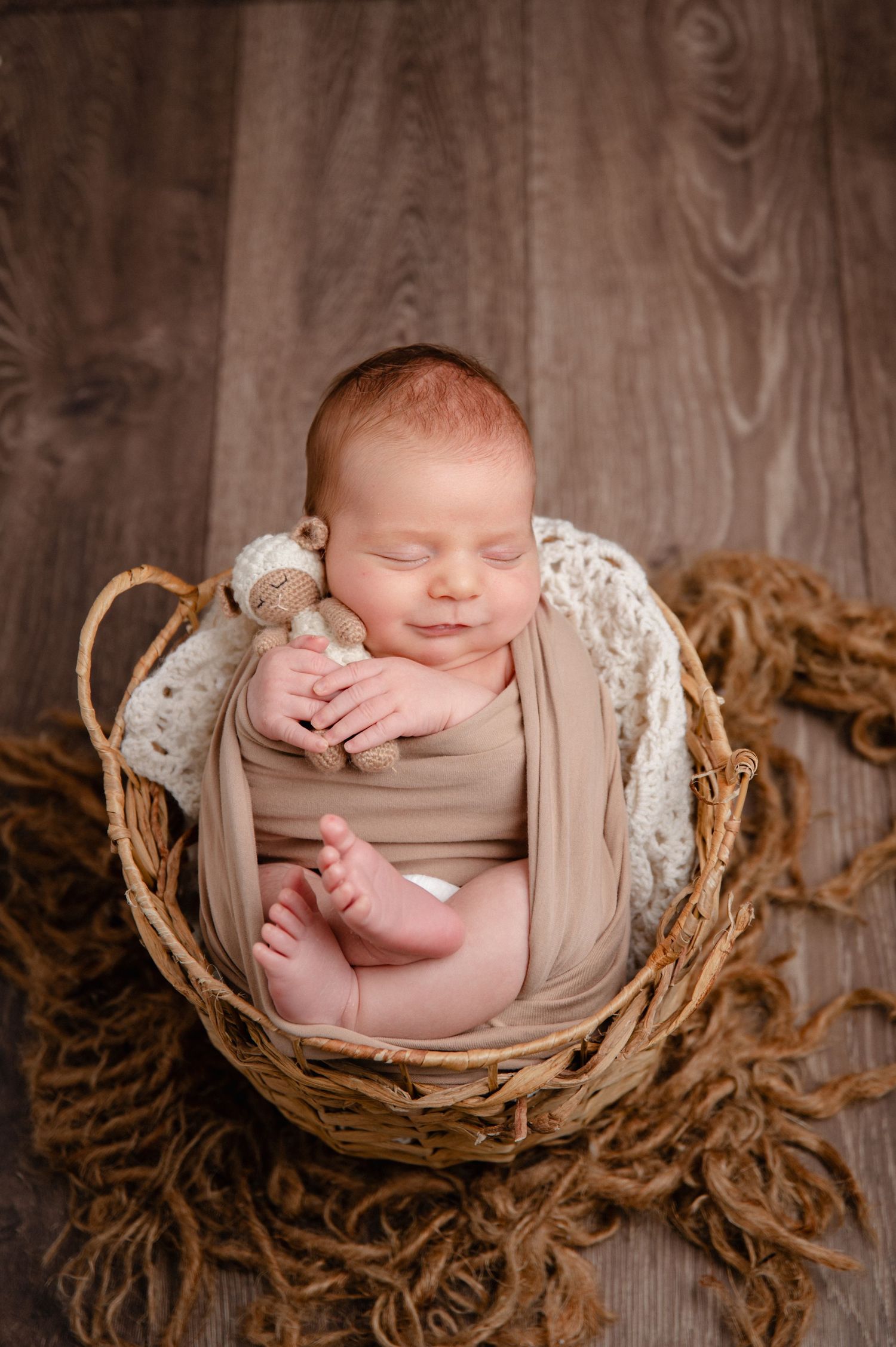 Sleeping newborn wrapped in tan fabric nestled in rustic woven basket.