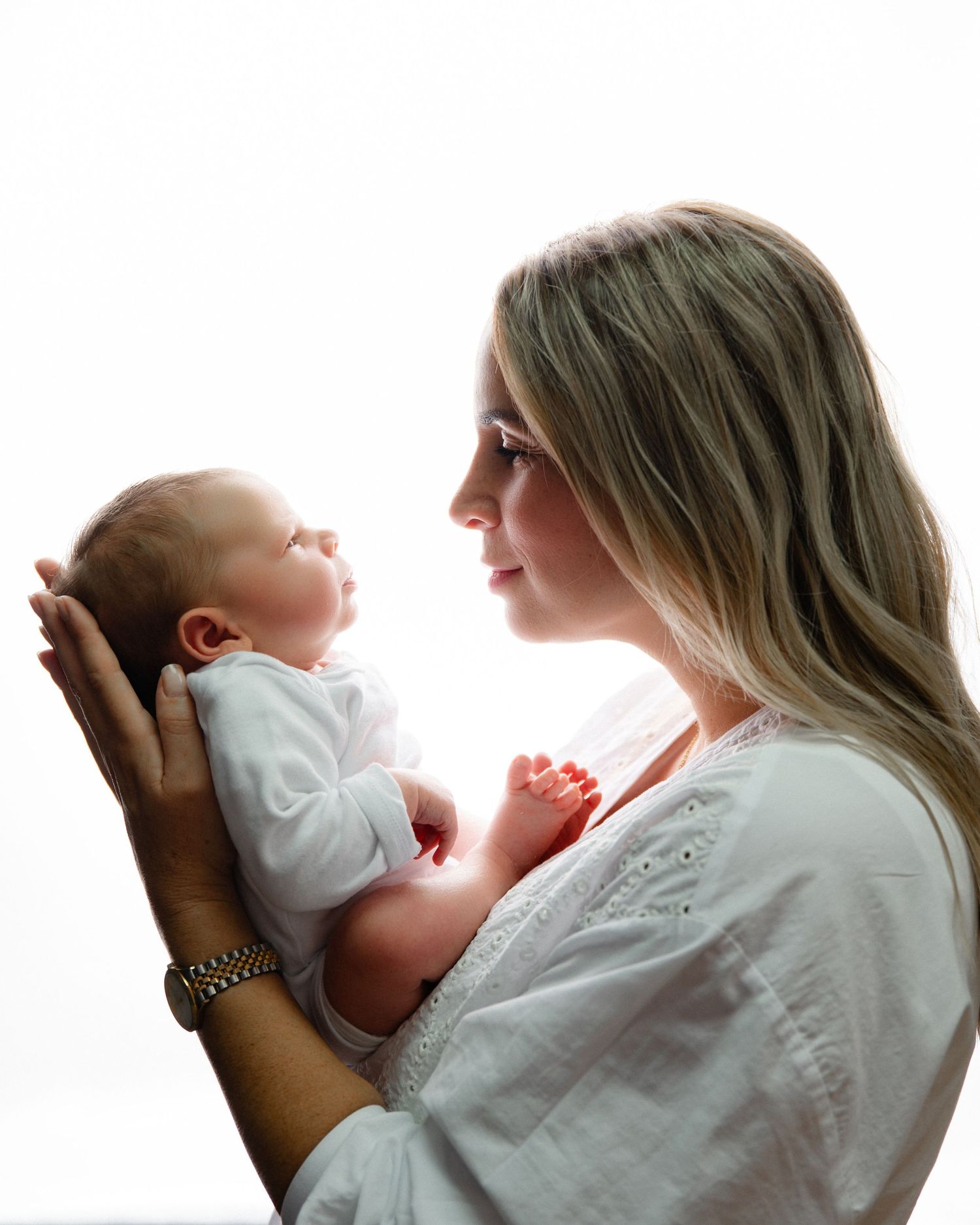 Side profile of parent and newborn sharing a tender moment against white background.