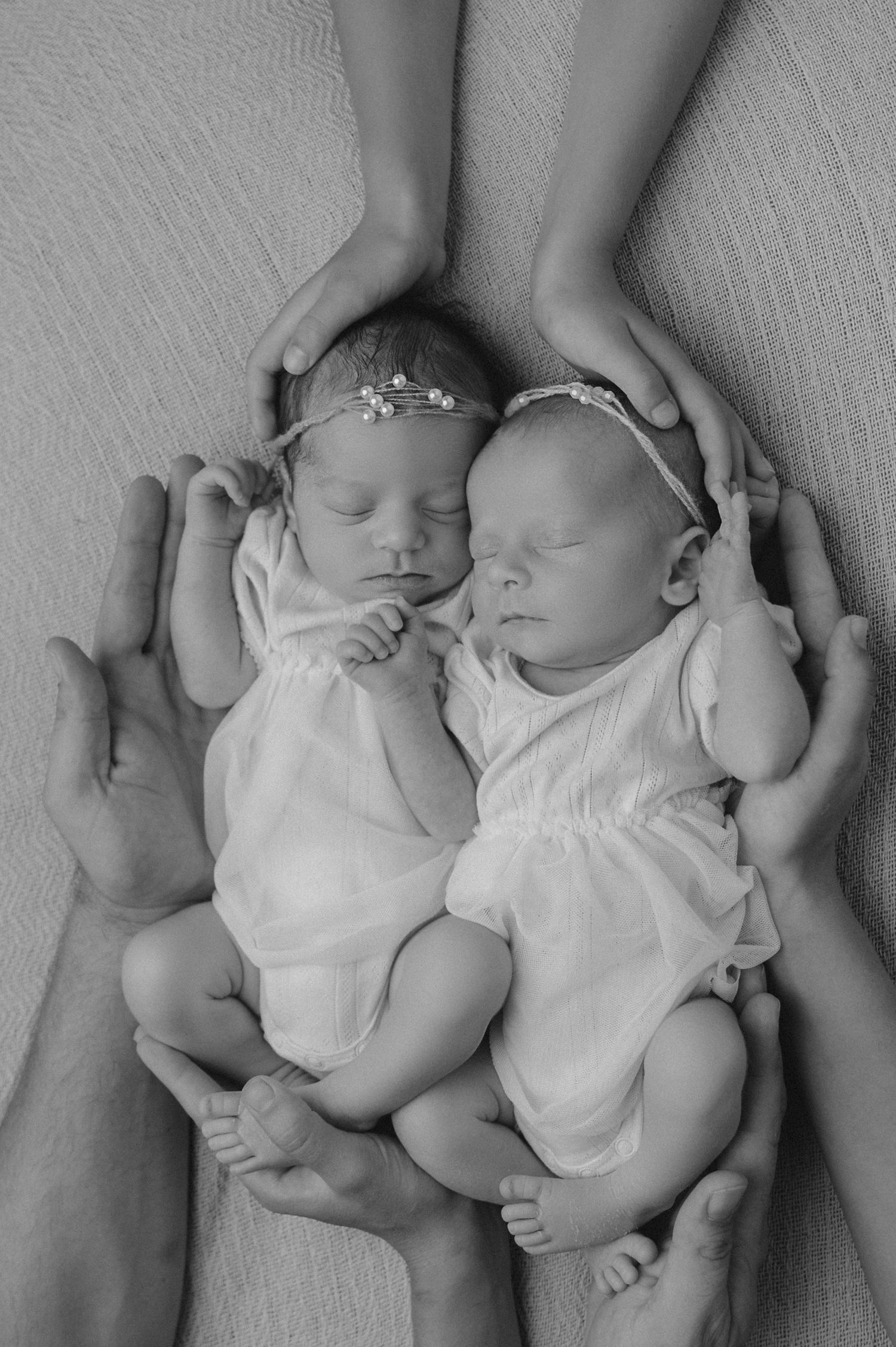 Black and white portrait of twin newborns sleeping side by side in matching outfits.