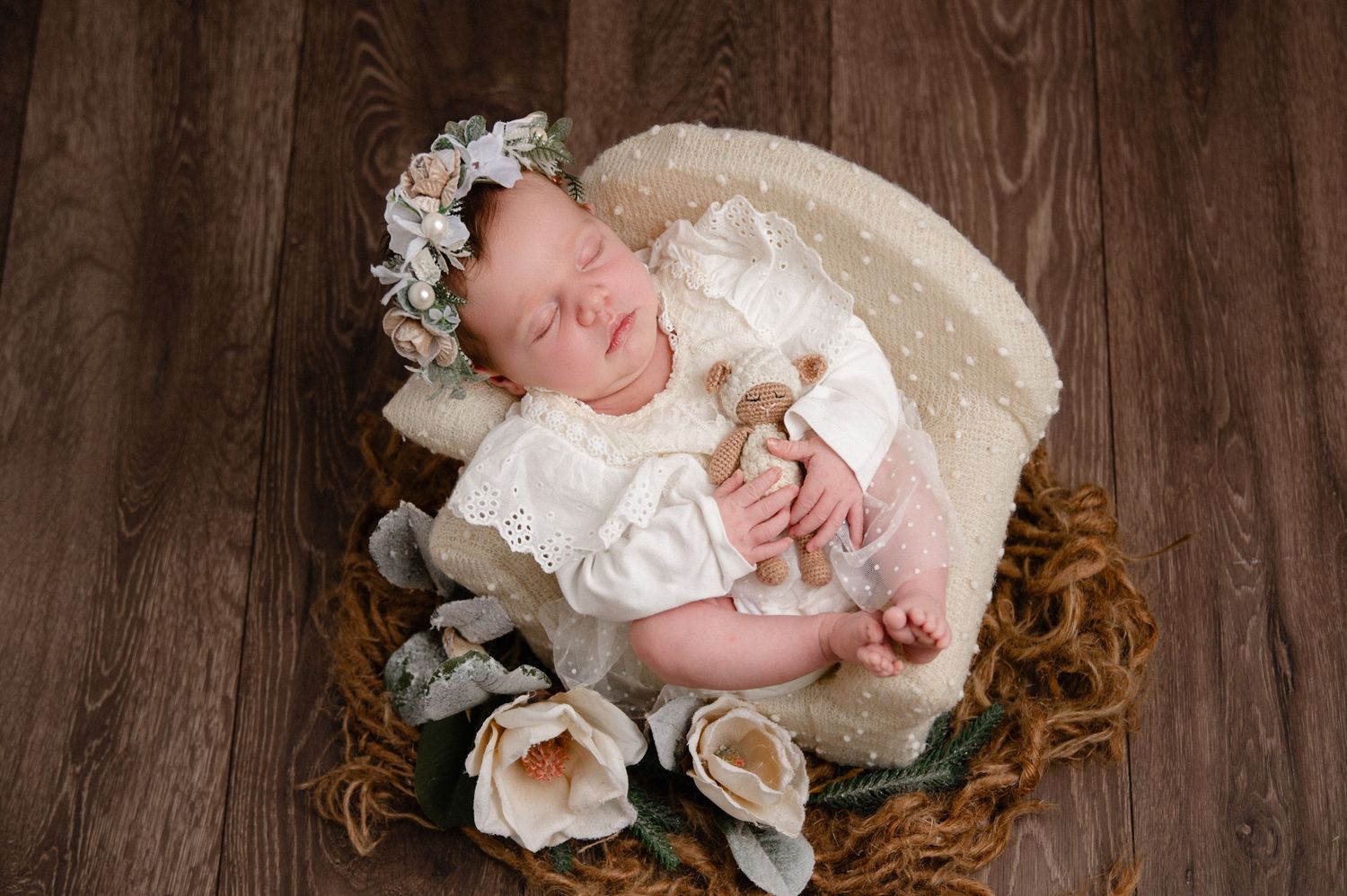 Newborn baby in vintage white lace dress sleeping on wooden floor with roses.