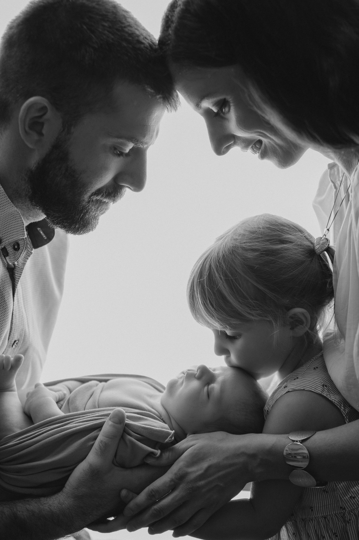 An intimate black and white photograph of a family gathered around their newborn sibling.