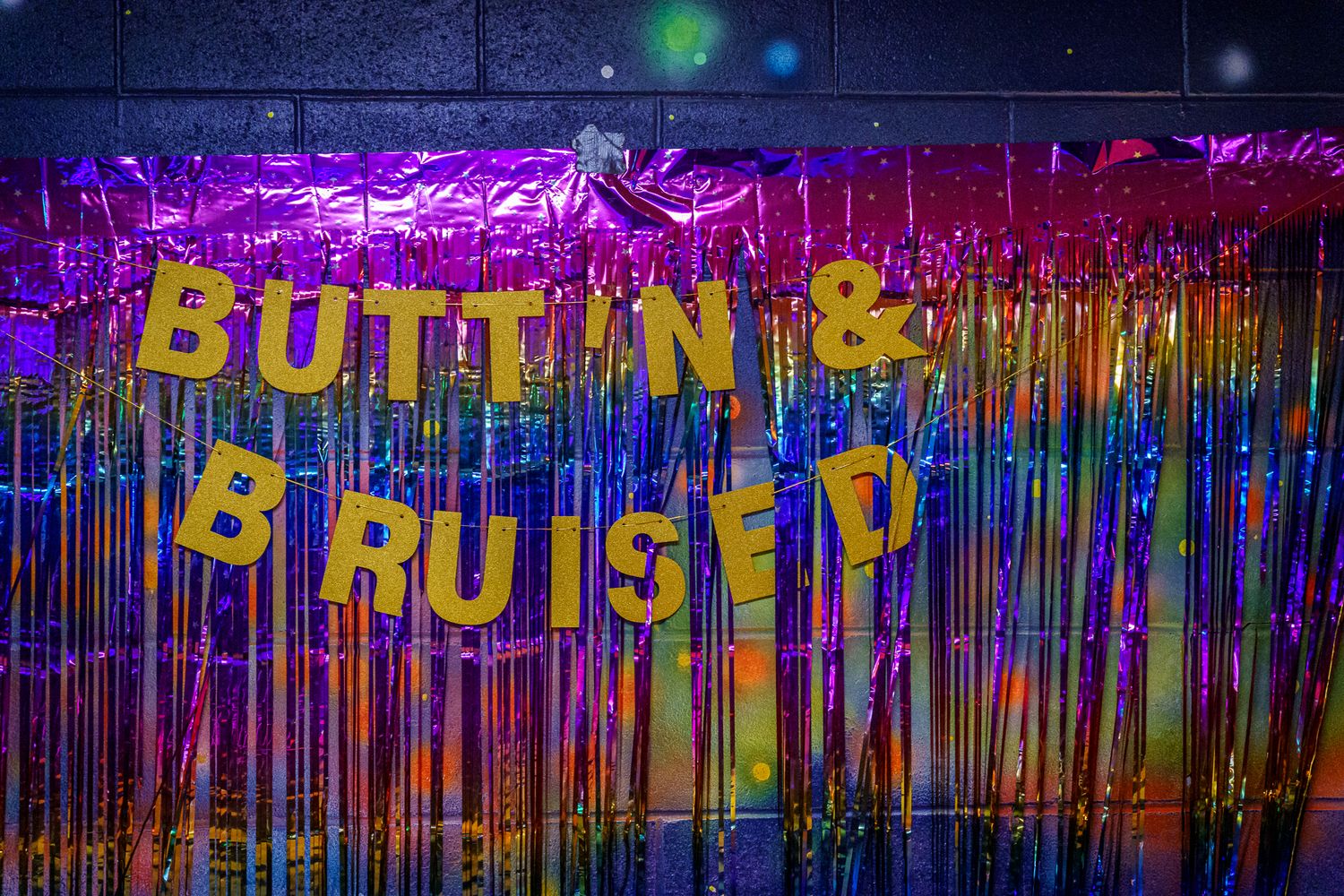 Colorful dripping paint artwork with gold 'Butt N & Bruised' text banner against vibrant purple and blue backdrop.
