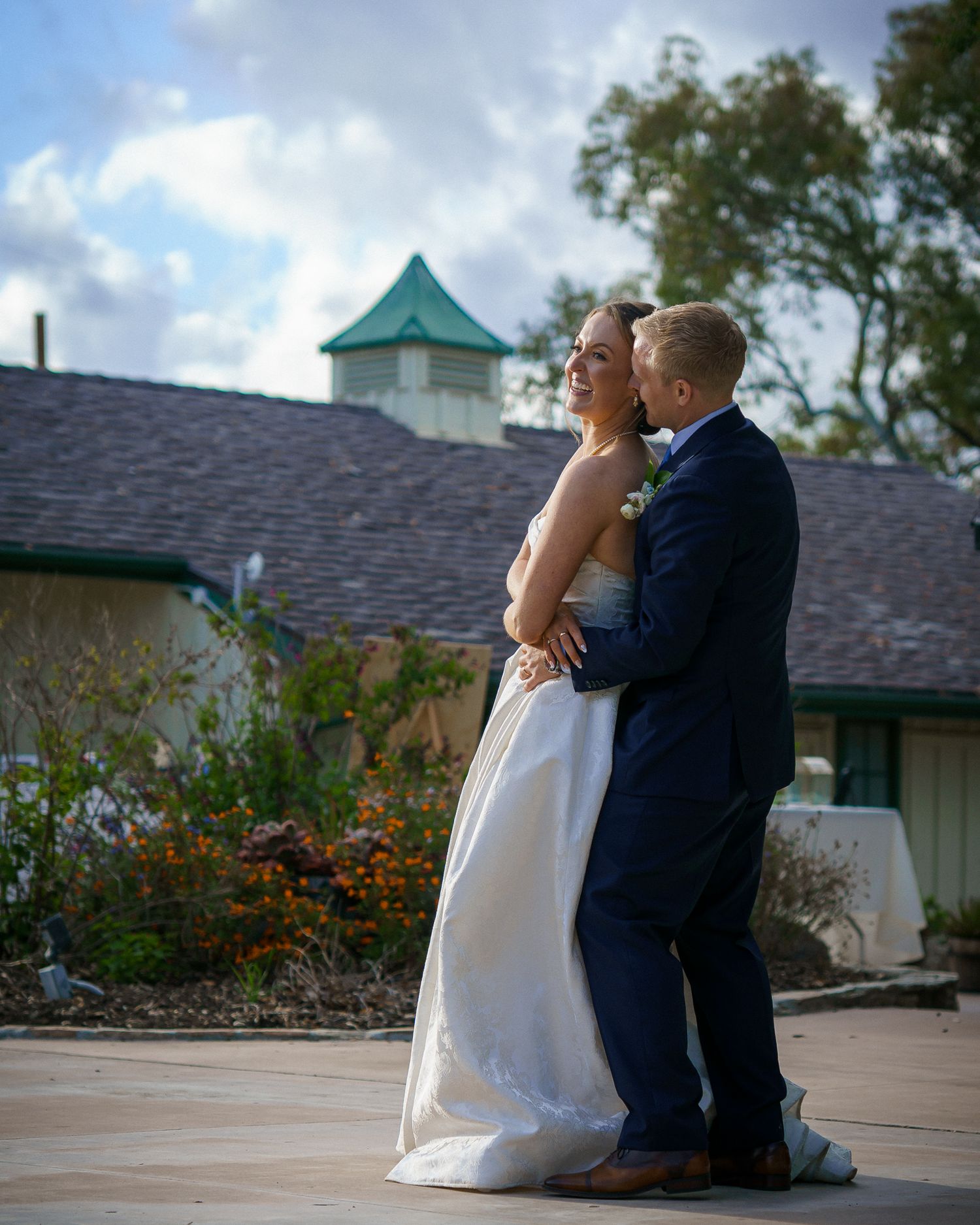 A couple shares an intimate moment at sunset outside a building with blue skies in the background.