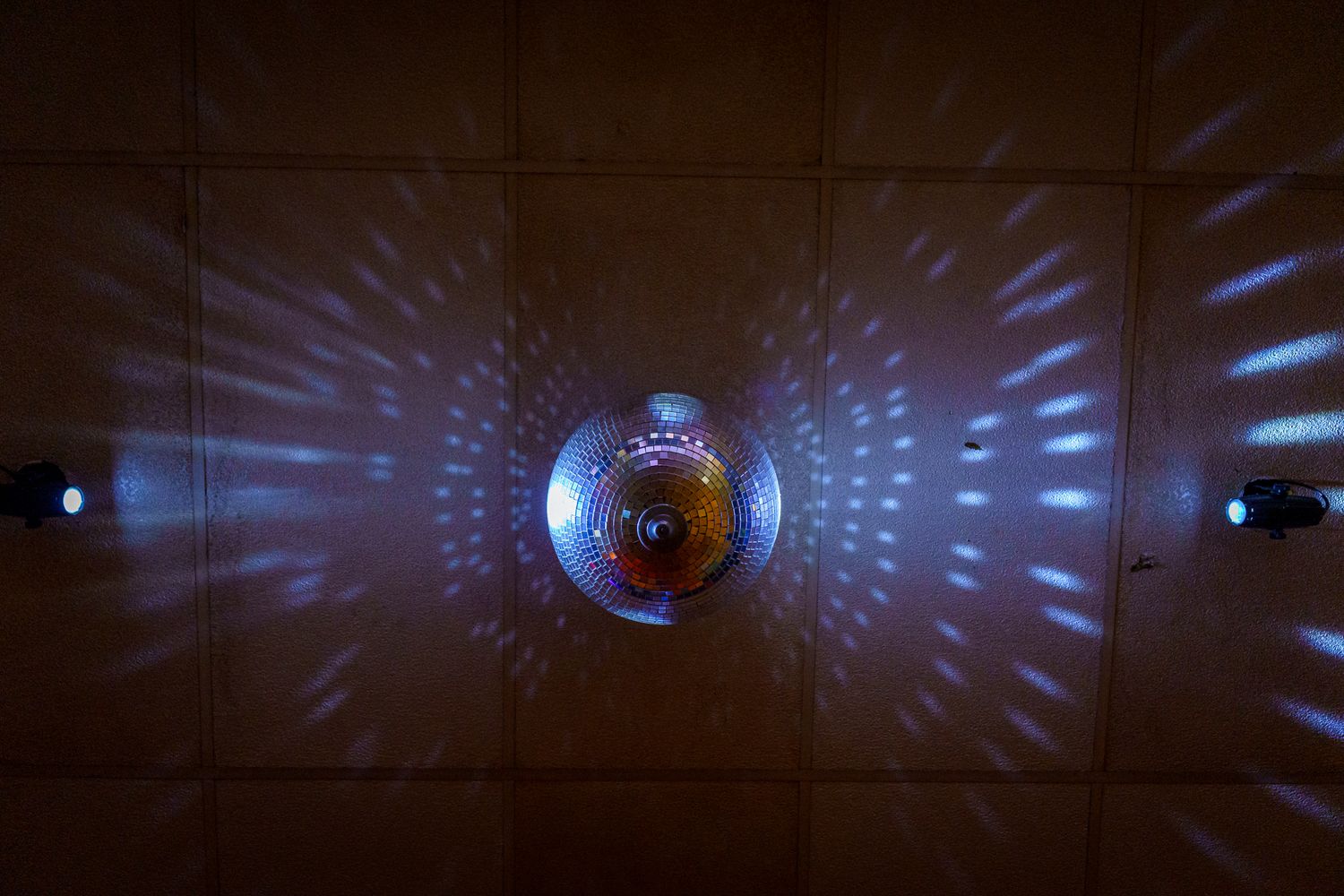 A disco ball creates a mesmerizing pattern of blue light reflections on dark walls in a dimly lit space.
