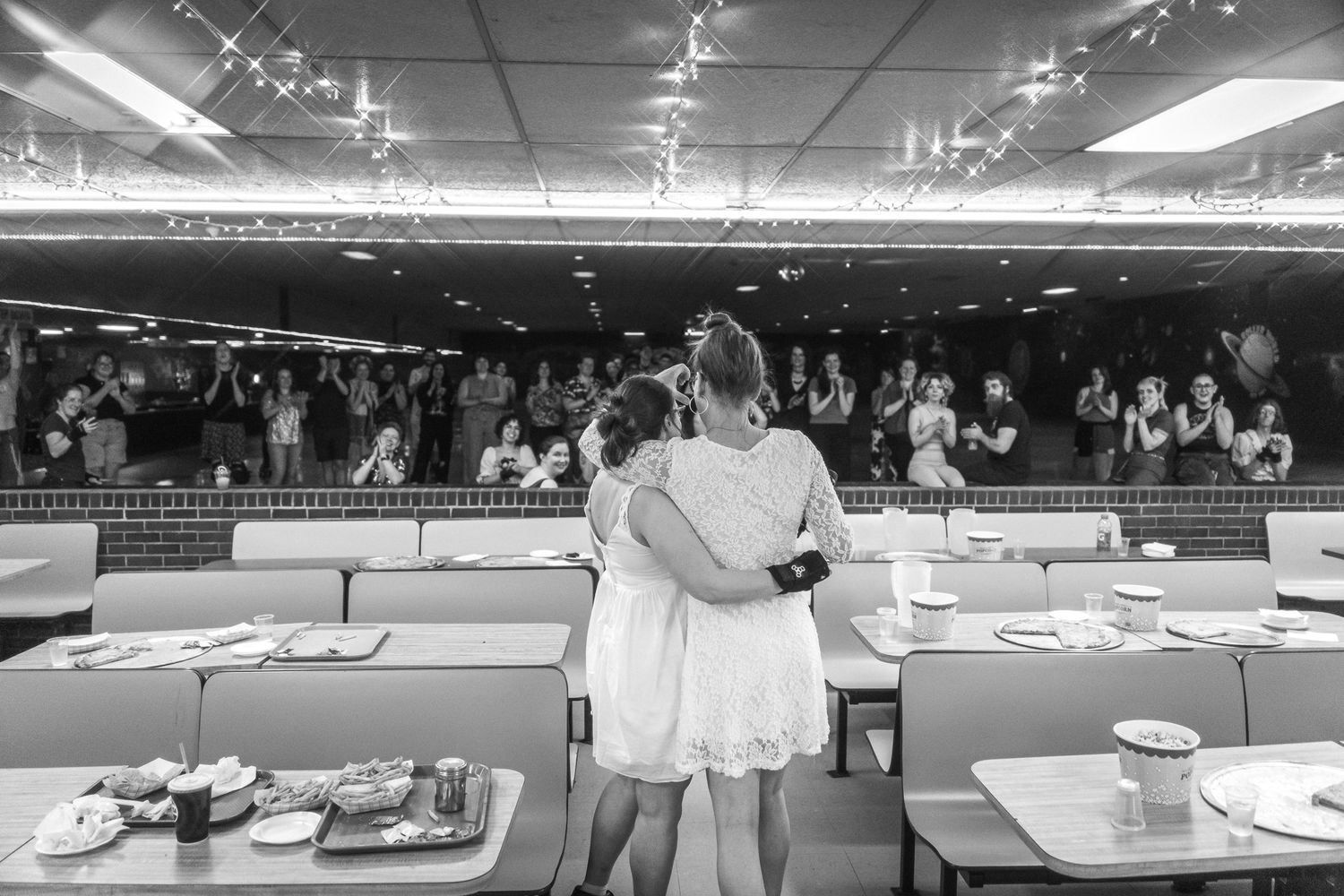 A black and white view of people standing at a large table display inside a brightly lit commercial space with cafe tables.