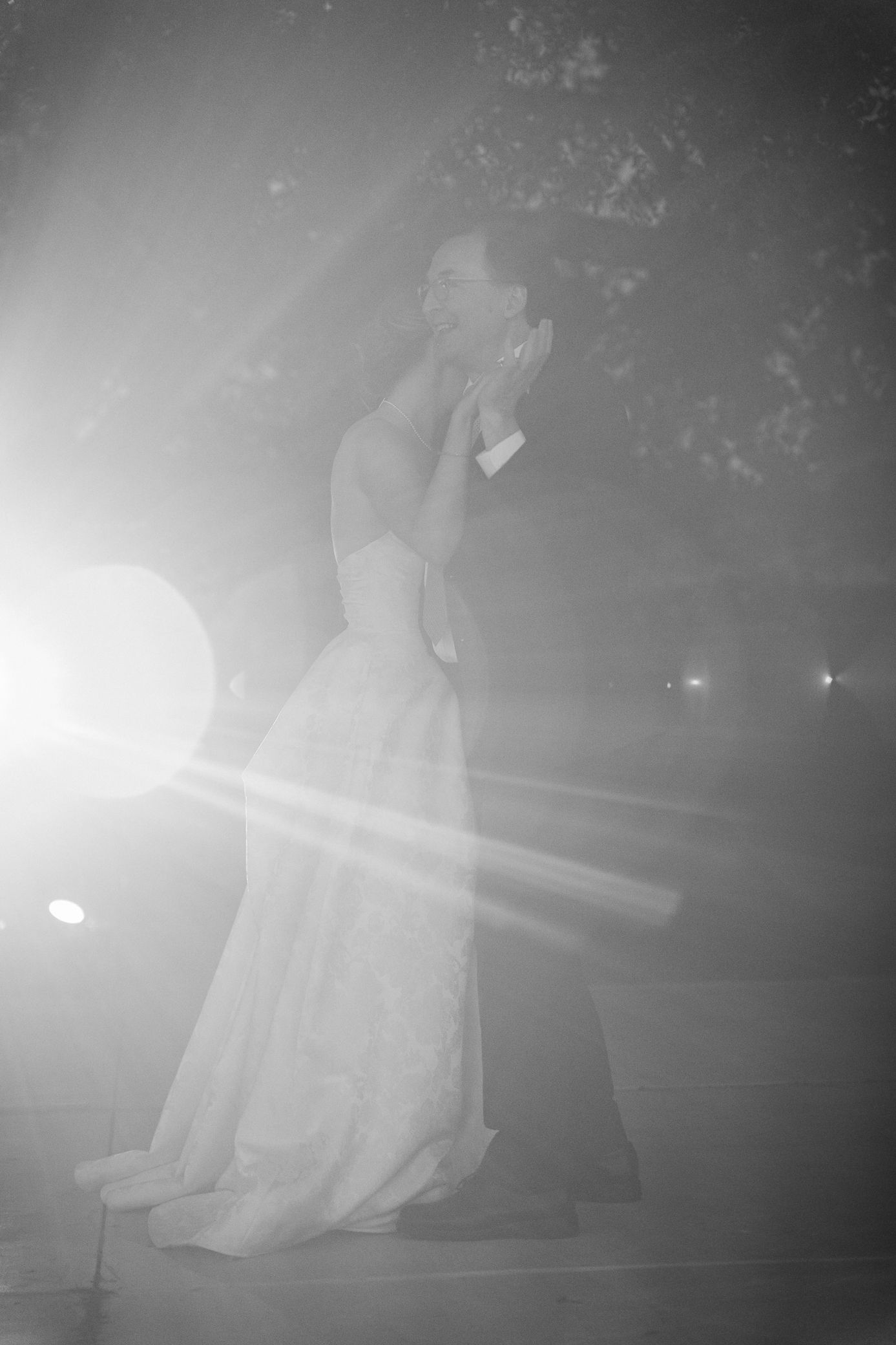 A performer in an elegant white dress poses dramatically on stage amid misty theatrical lighting and lens flares.