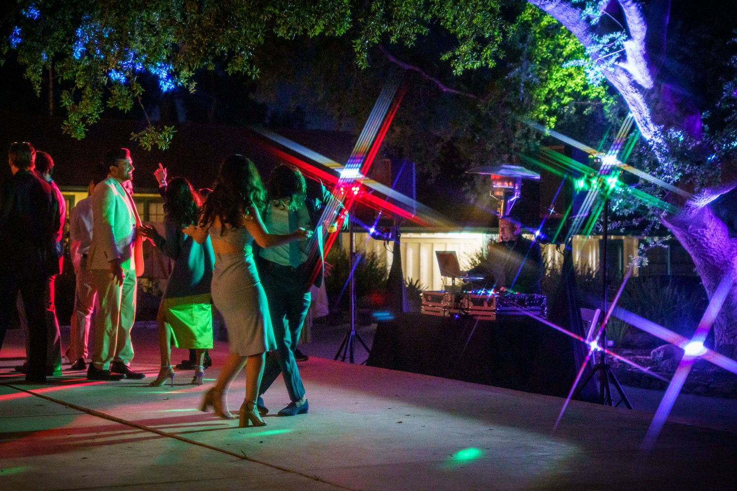 People dancing at an outdoor nightclub party with colorful neon lights and dance floor illumination.