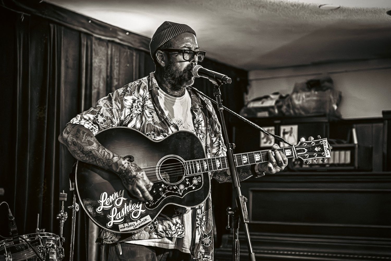 Musician performing with an acoustic guitar in a casual venue, captured in dramatic black and white lighting.